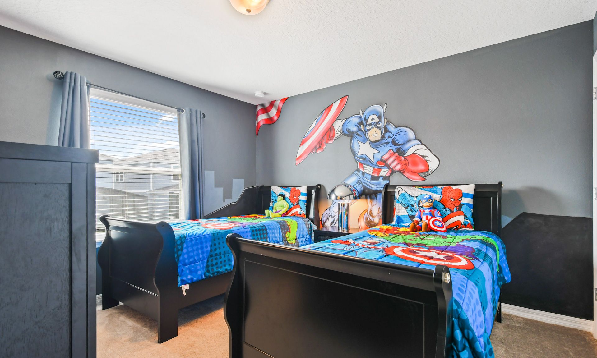 Superhero-themed kids' room with twin beds, vibrant bedding, and dynamic wall art featuring Captain America.