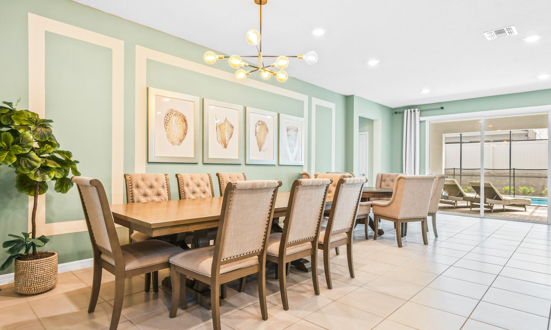 Elegant dining room with seating for 14, chic wall art, modern chandelier, and poolside views.