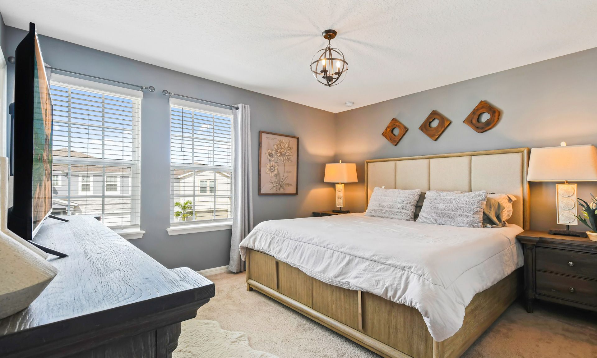 Cozy bedroom with king bed, stylish decor, ample natural light, and a large flat-screen TV for comfort.