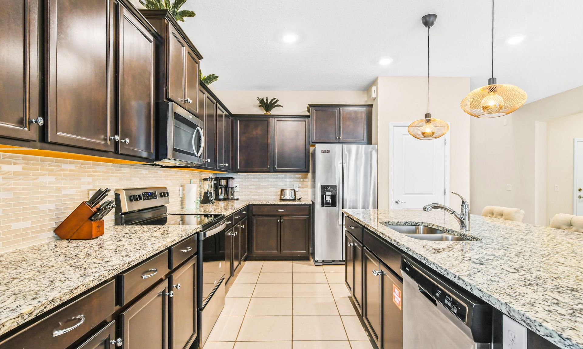 Modern kitchen with granite countertops, stainless steel appliances, dark cabinets, and chic lighting.