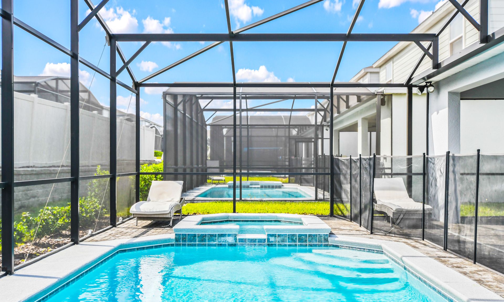 Private screened-in pool and spa with safety fence, sunny lounge area, and clear blue skies above.