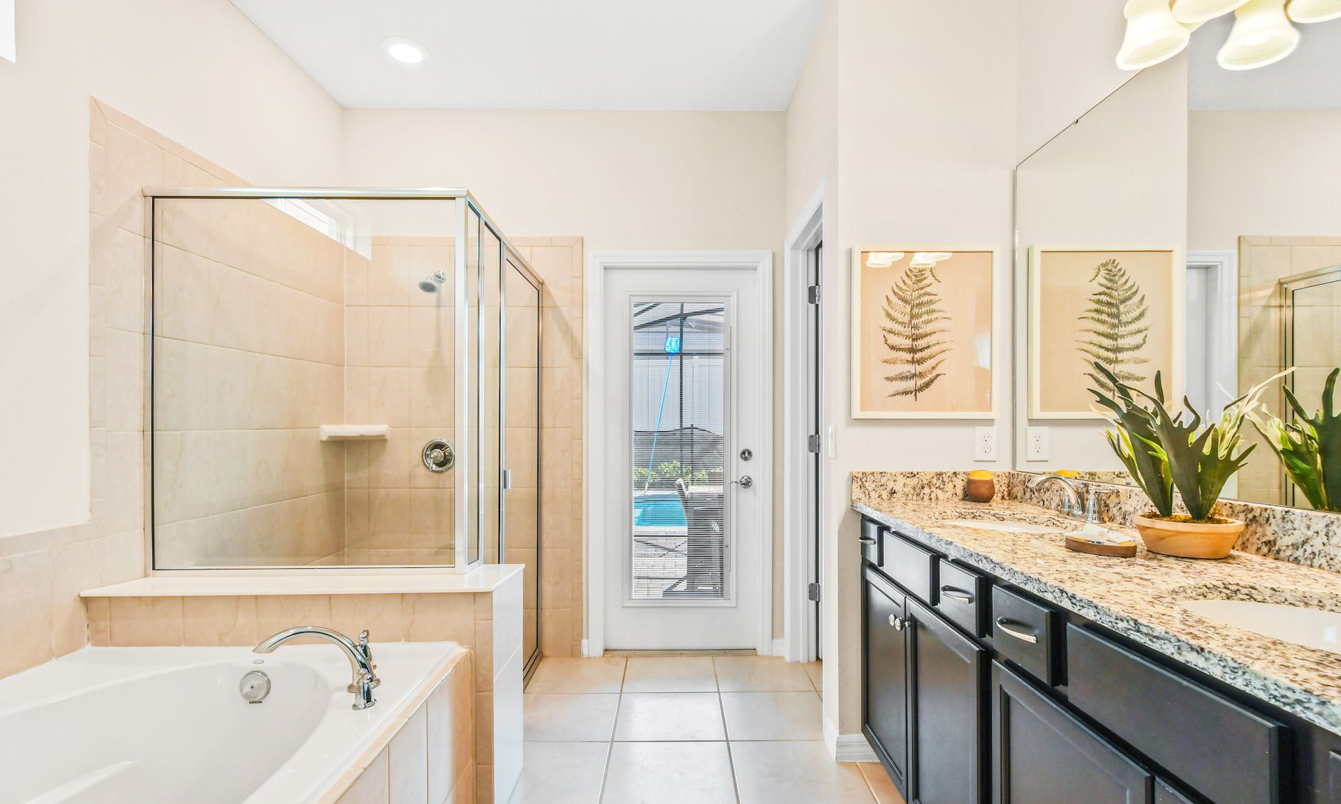 Luxurious bathroom with a glass shower, soaking tub, double granite vanity, and direct pool access.