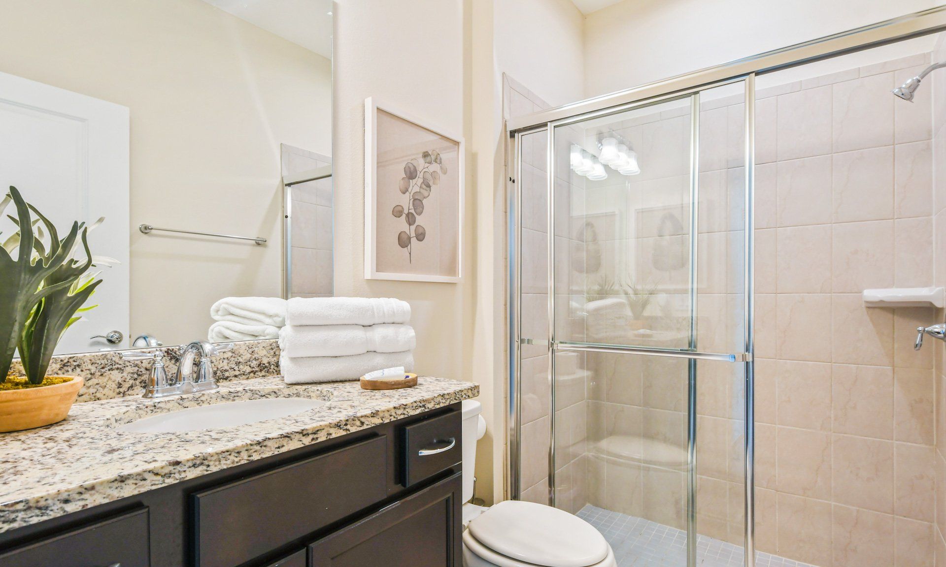 Stylish bathroom with granite vanity, glass-enclosed shower, fresh towels, and modern decor accents.