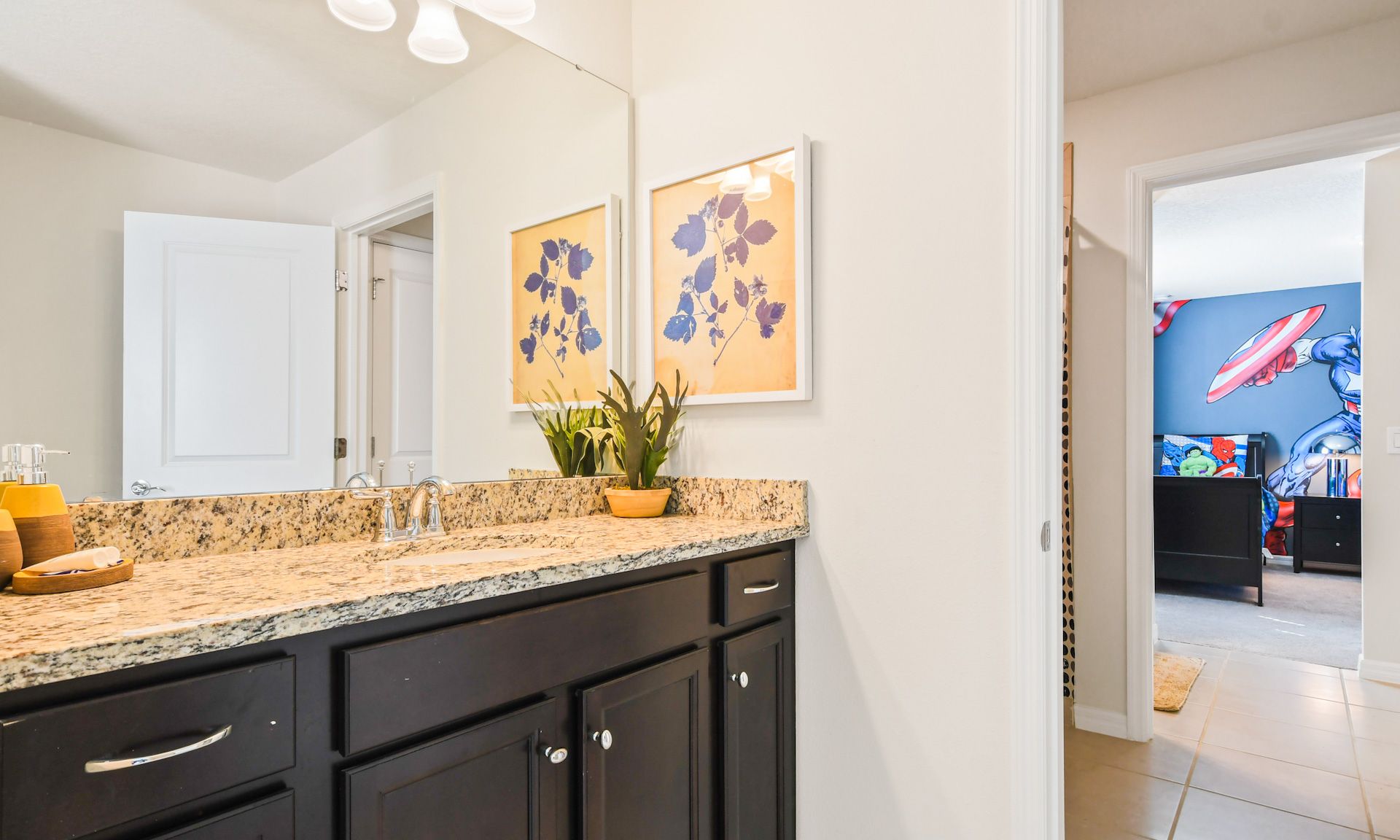 Modern bathroom with granite countertop, vibrant floral decor, and access to the superhero-themed bedroom.