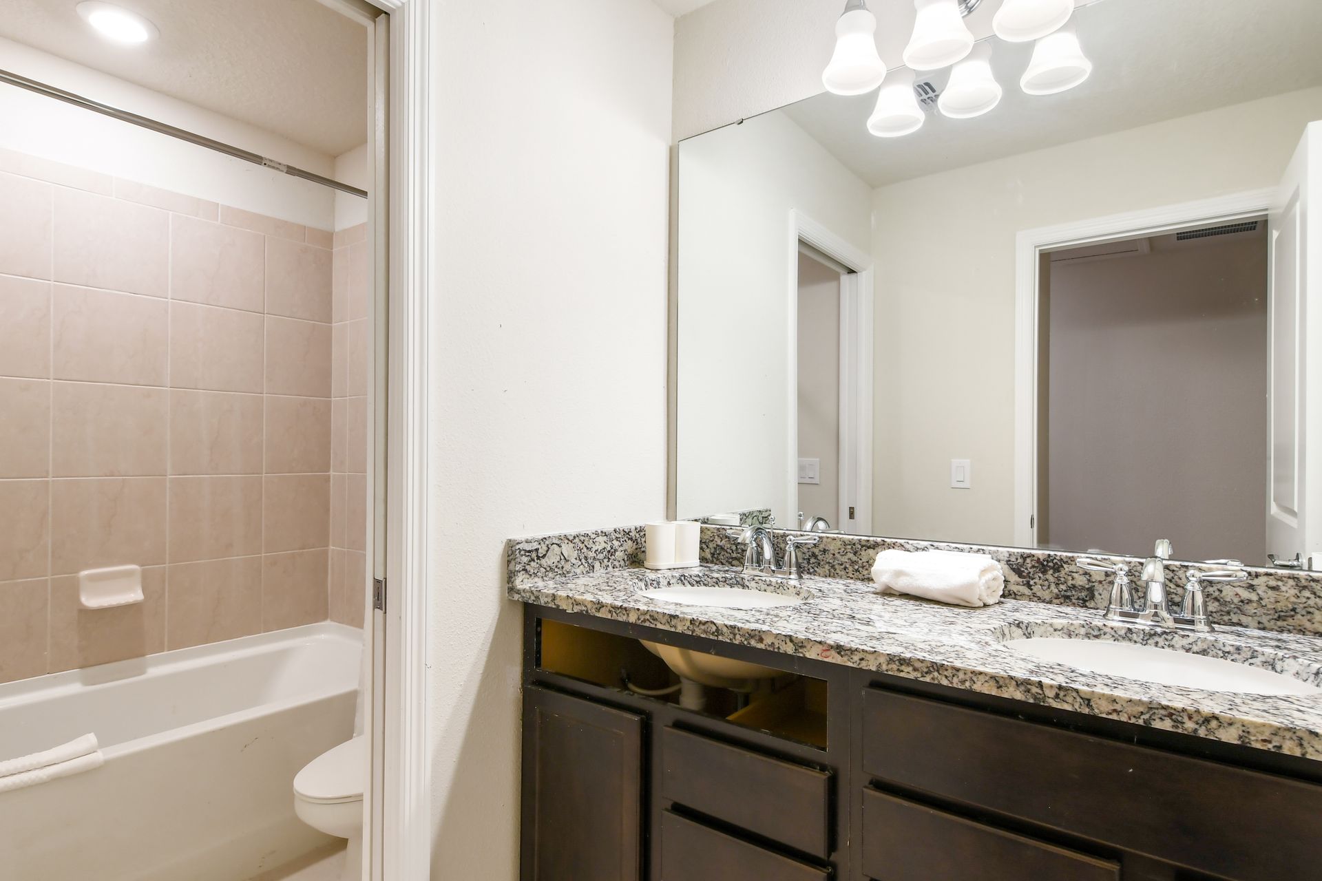 Bright modern bathroom with double granite sinks, large mirror, and tiled shower