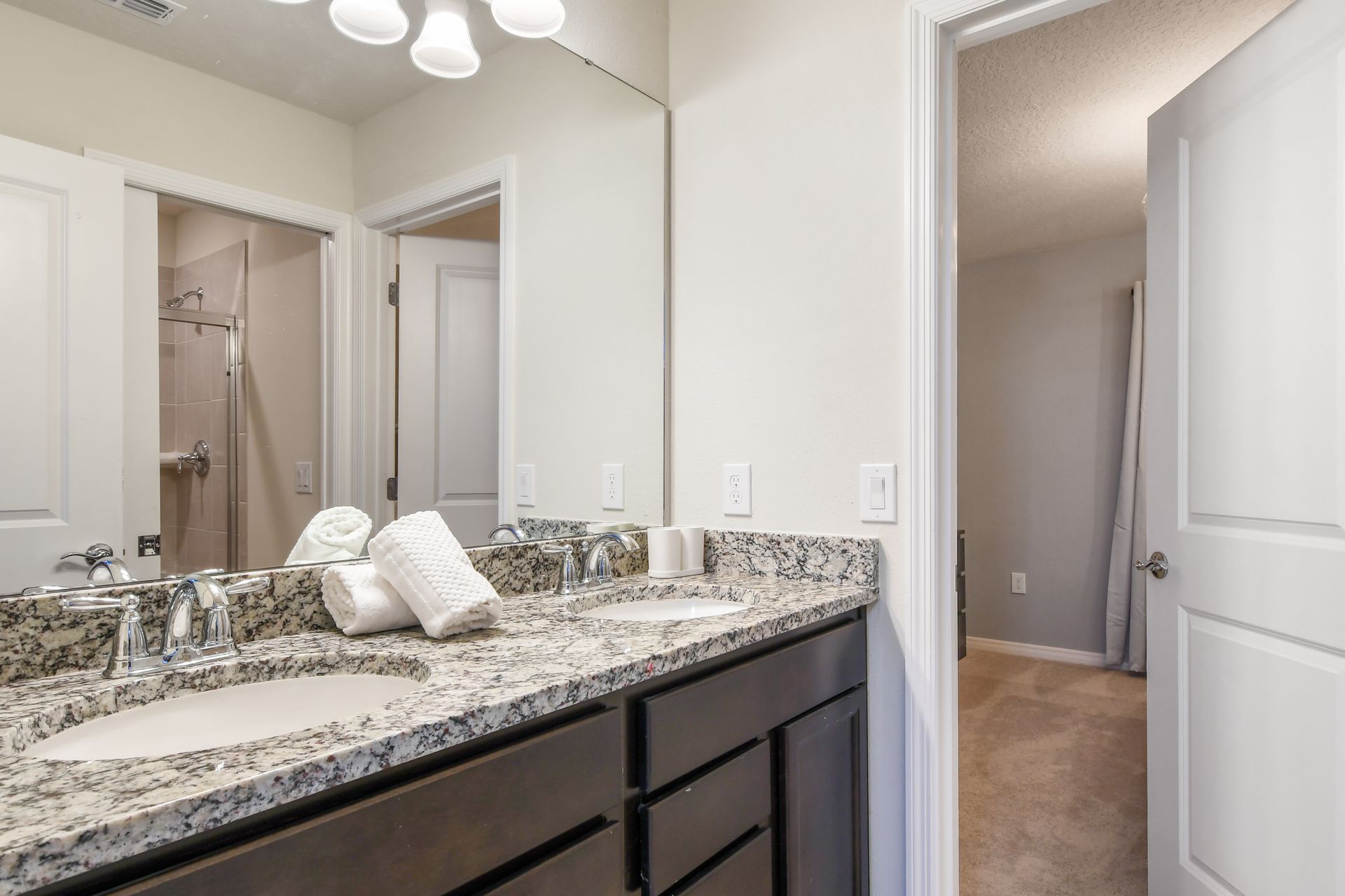 Bright bathroom with double granite vanity, large mirror, and walk-in shower nearby