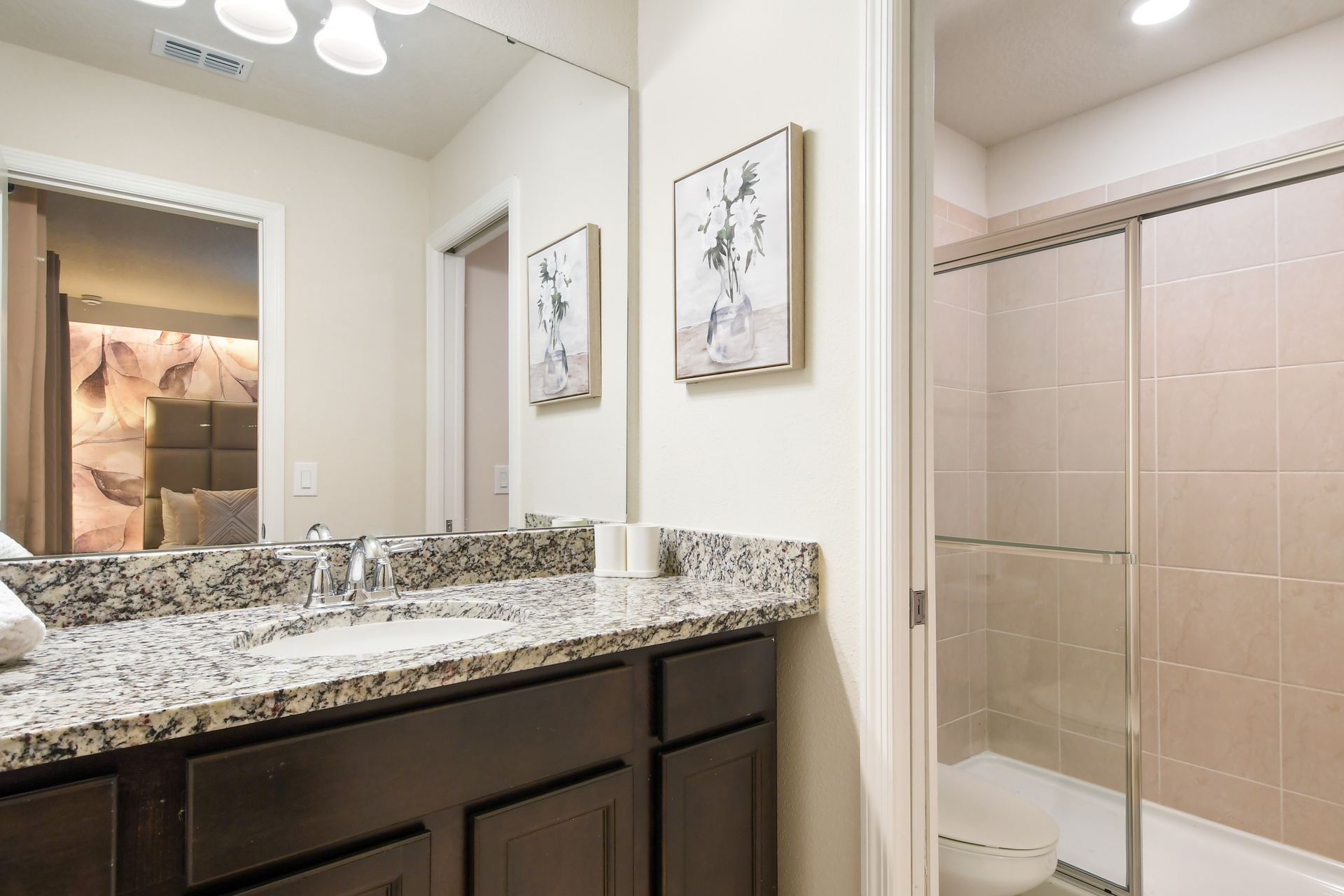 Chic bathroom with granite vanity, glass shower, soft lighting, and cozy bedroom view