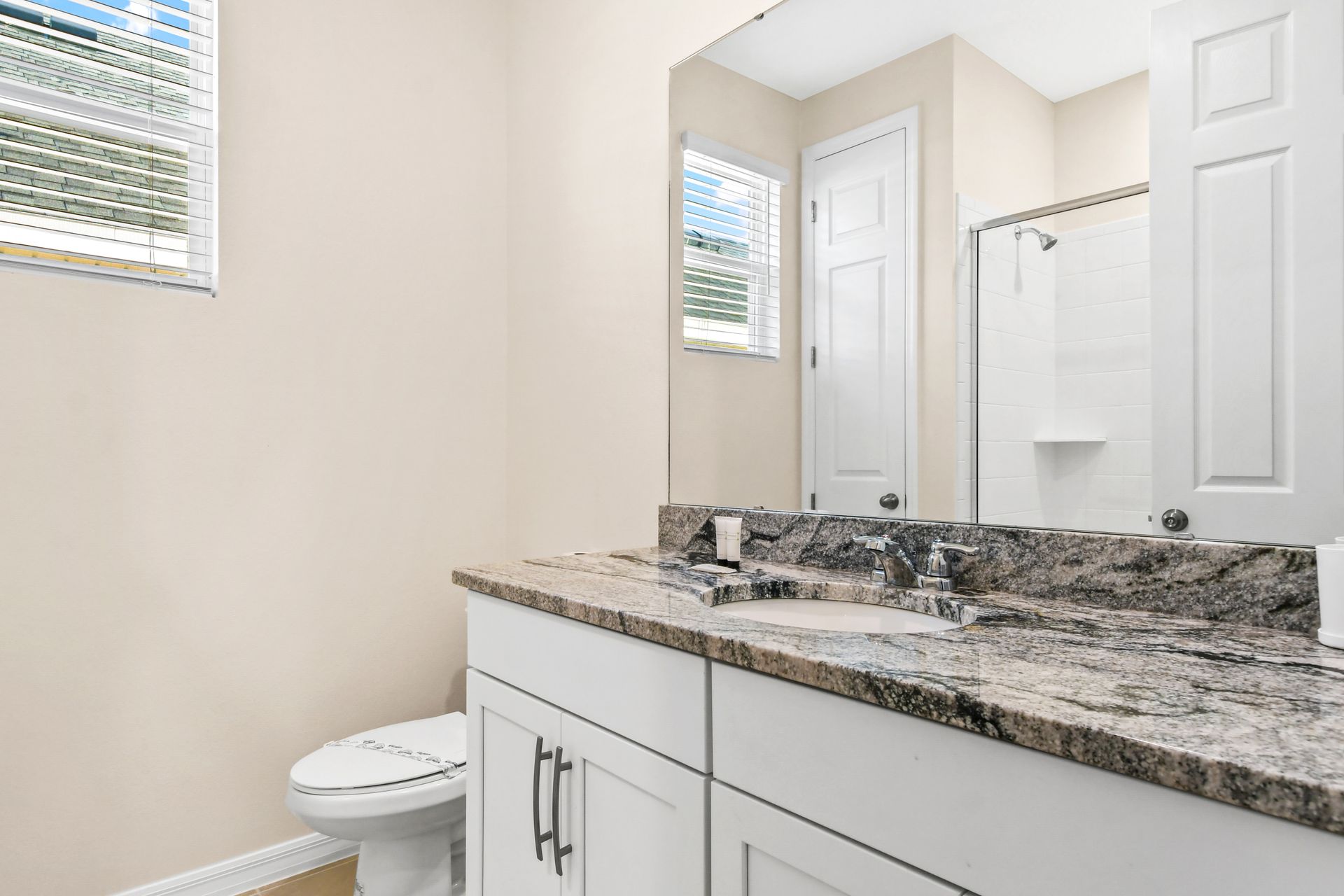 Modern bathroom with granite counters, bright window, and shower.