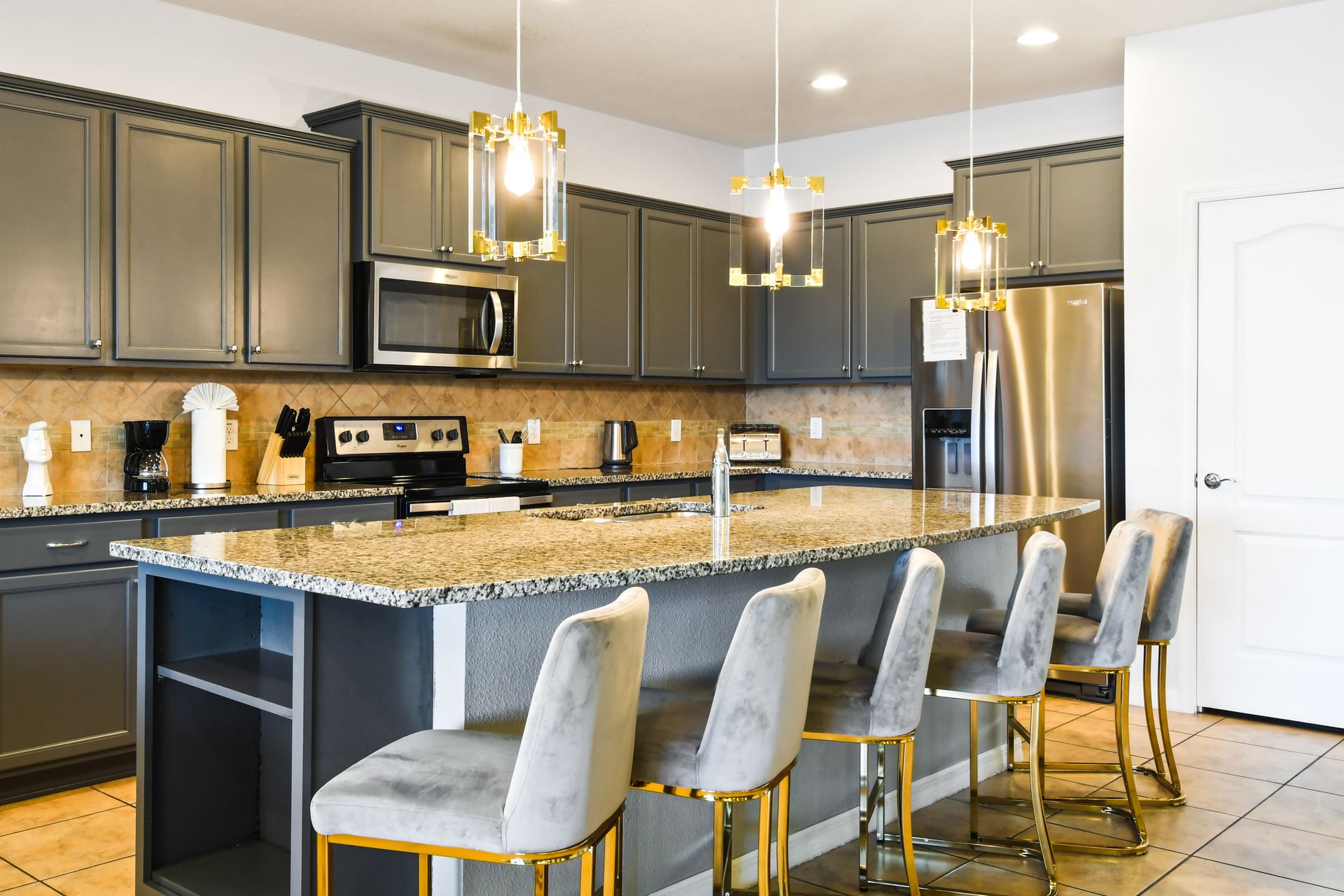 Modern kitchen with granite counters, stainless steel appliances, and gold lighting.