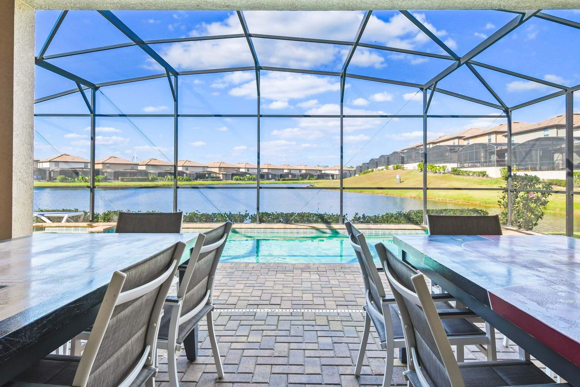 Serene lakefront patio with screened pool, outdoor dining, and scenic open skies.