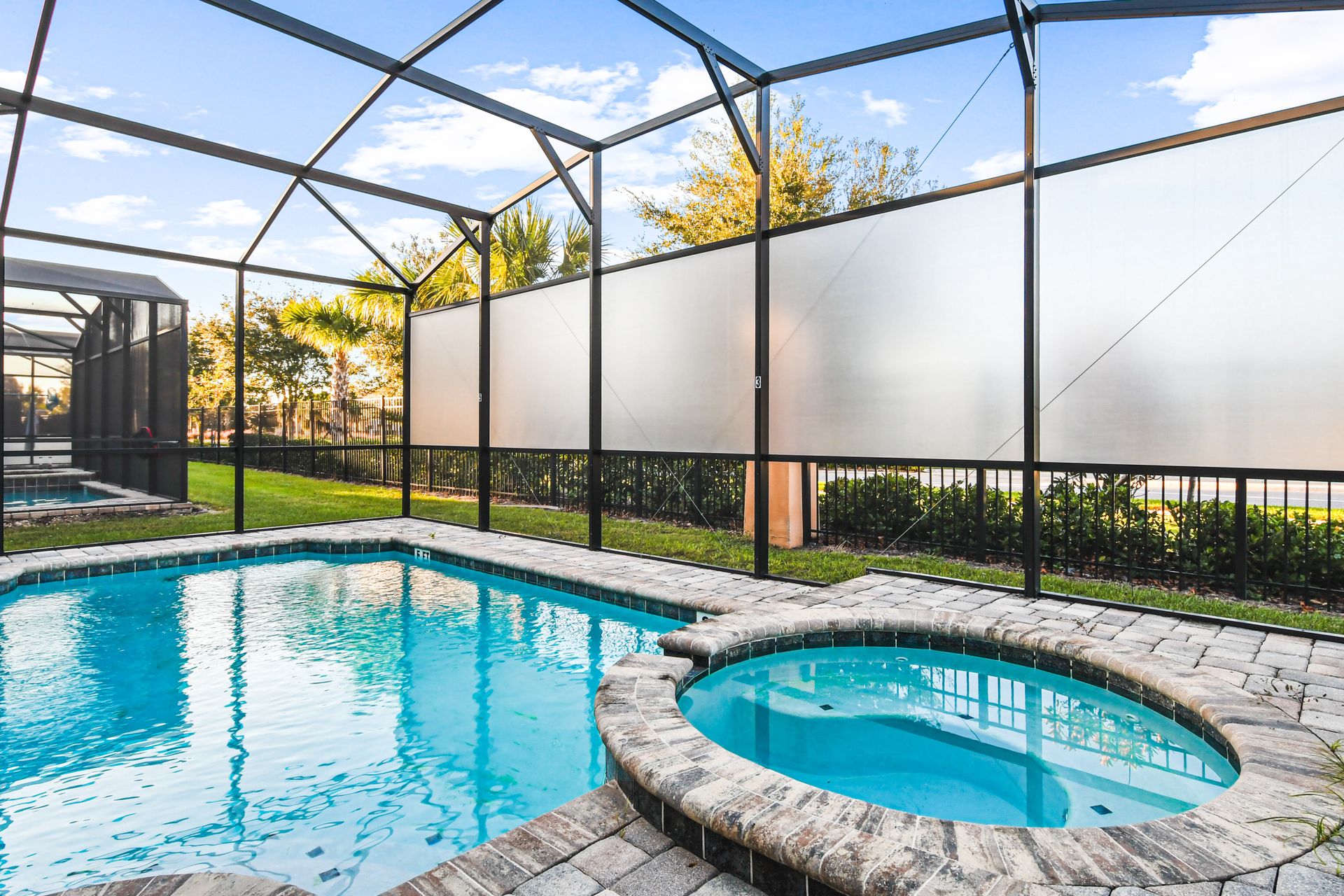 Screened-in pool and spa with safety fence, lounge chairs, and sunny patio space.