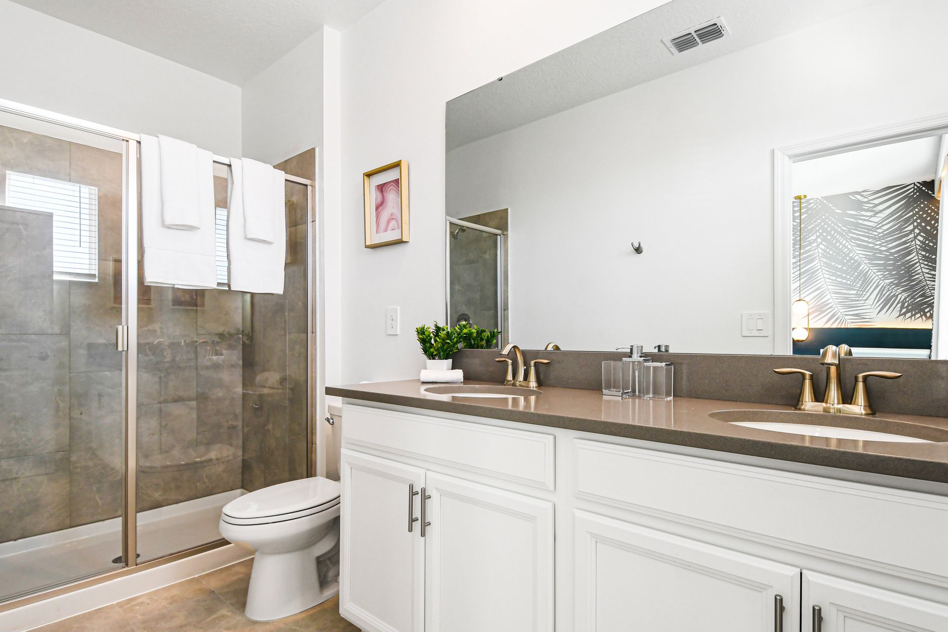 Bright bathroom with dual sinks, walk-in shower, and elegant gold fixtures.
