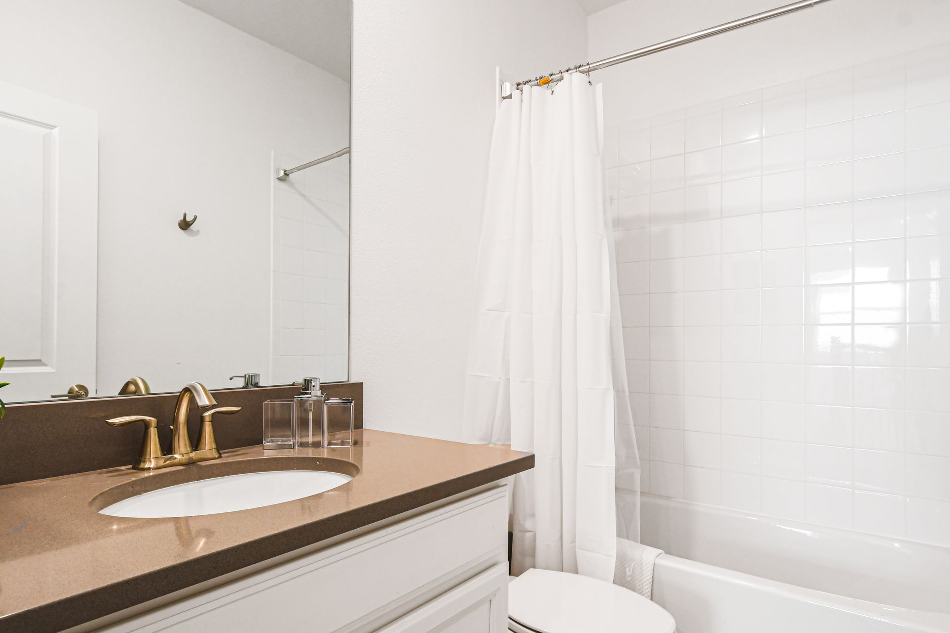 Sleek and clean bath with warm tones, white tile, and fresh greenery.