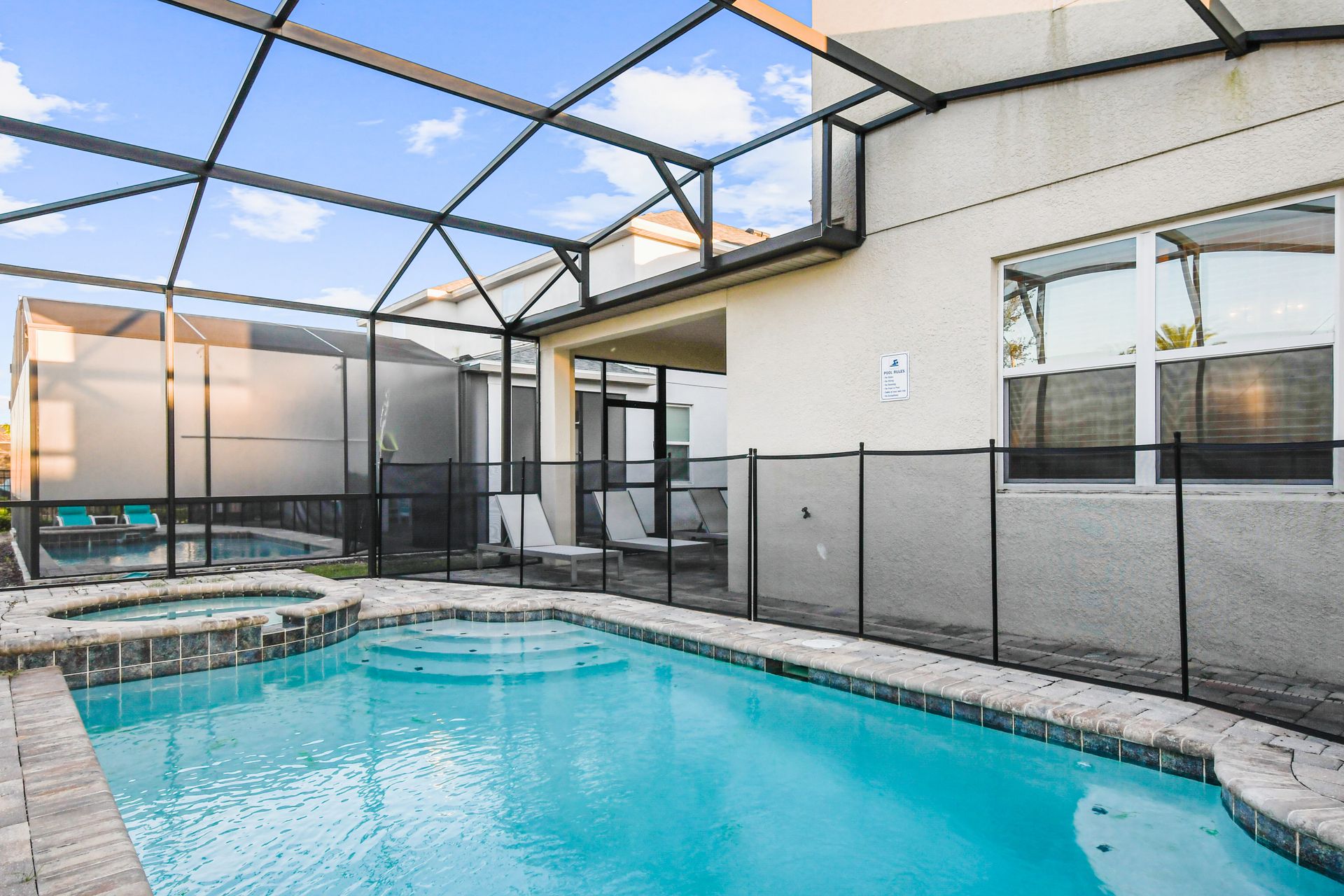 Screened-in pool and spa with safety fence, lounge chairs, and sunny patio space.