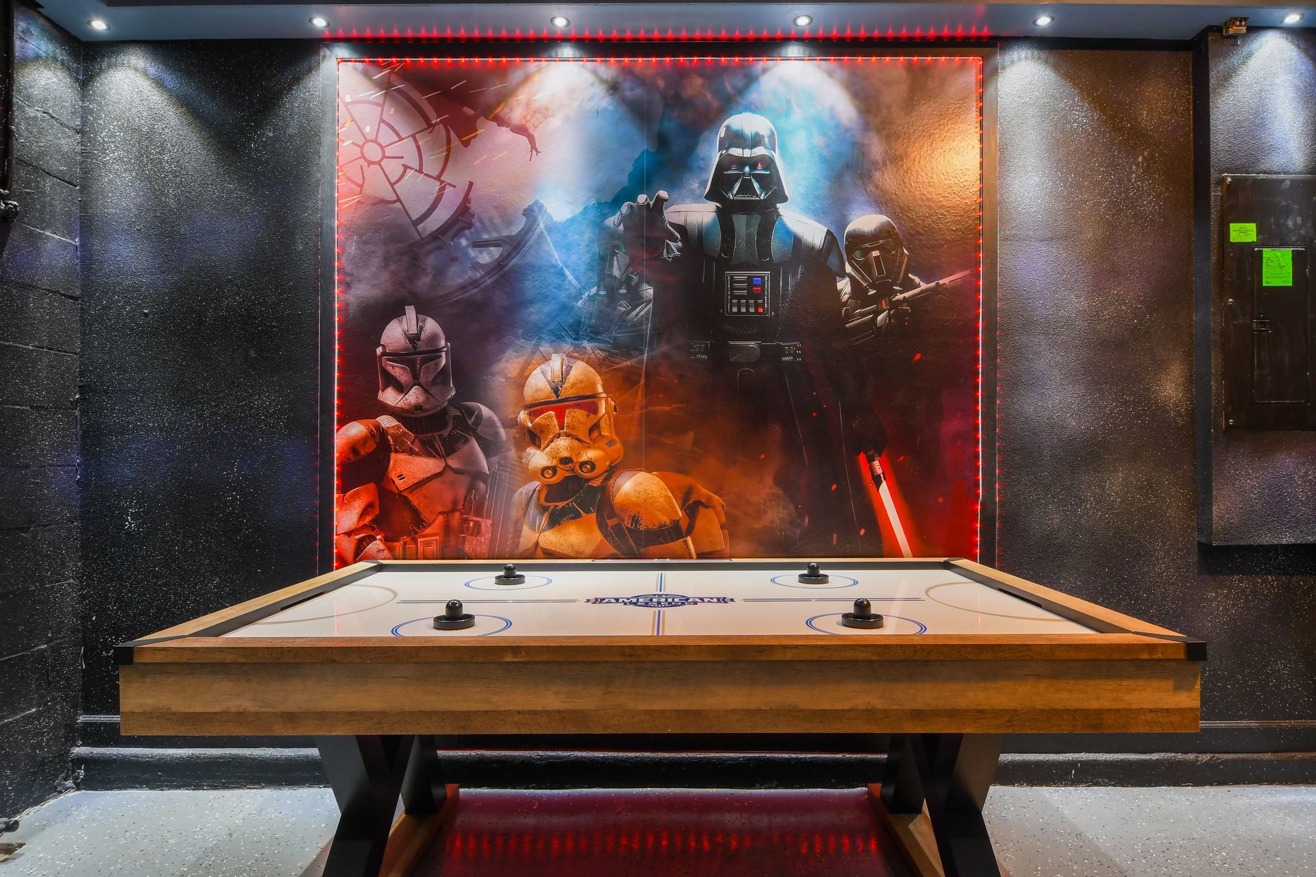 Star Wars-themed game room with epic mural, glowing lights, and air hockey action.