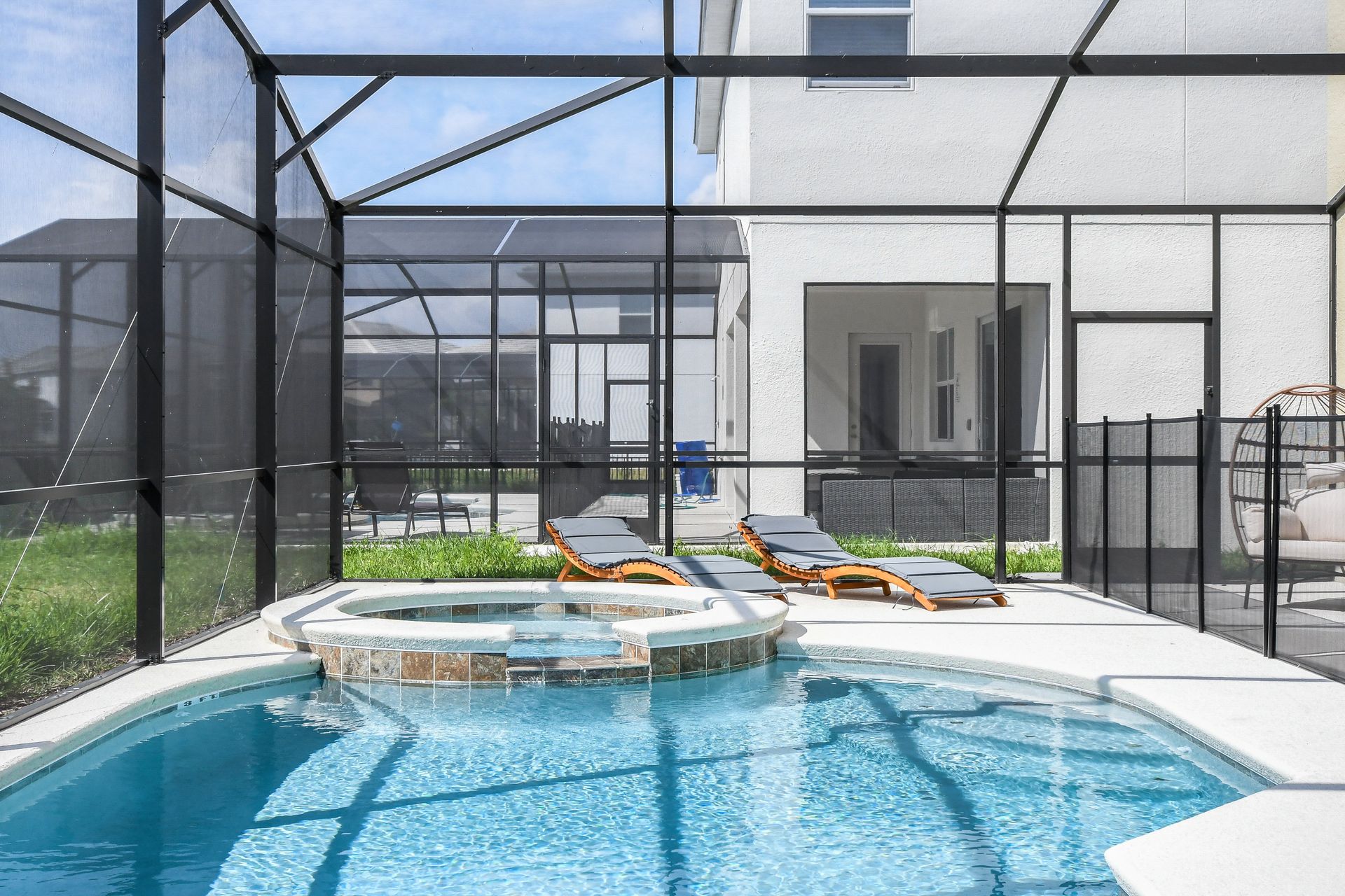 Screened-in pool area featuring a spa, cozy loungers, and a stylish hanging chair.