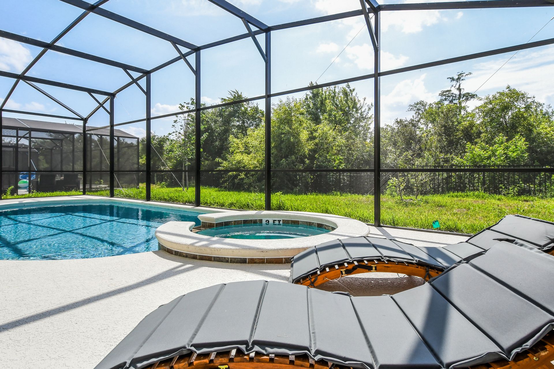 Screened-in pool and spa with lush greenery, sunny skies, and cozy loungers.
