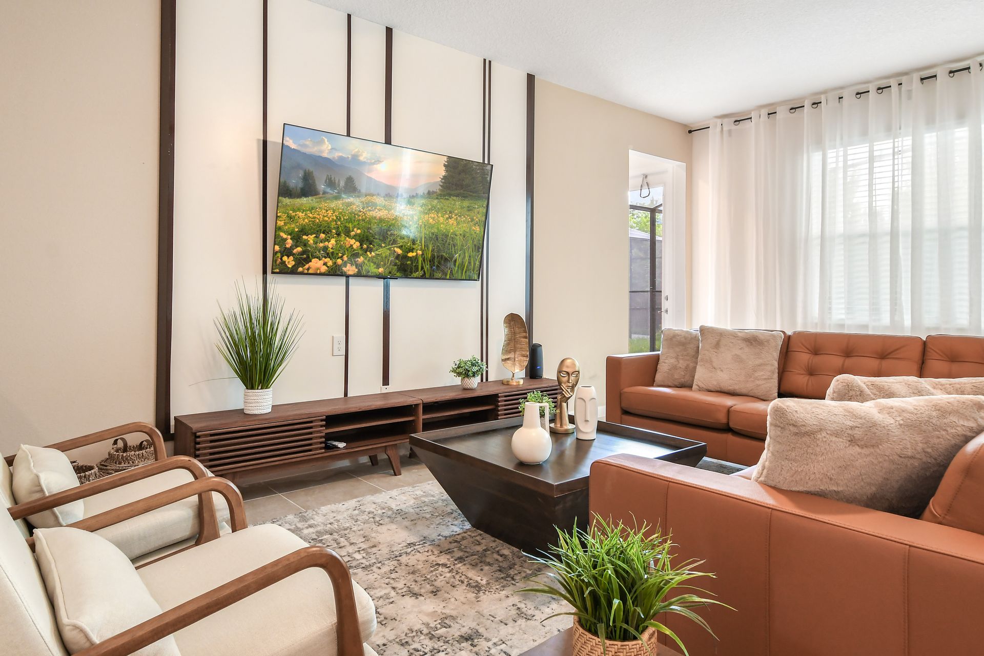 Stylish living room with warm leather seating, airy curtains, and a nature-inspired TV.