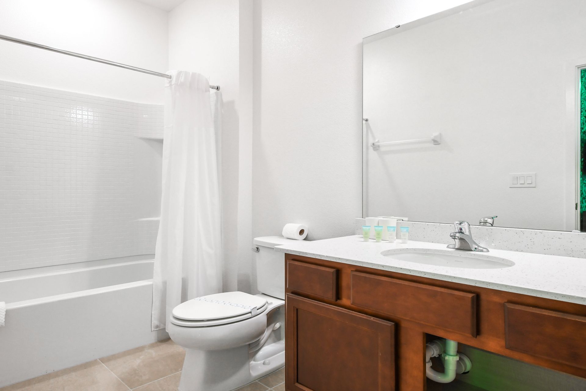 Modern bathroom with a tiled shower/tub, wooden vanity, and a bright quartz countertop.