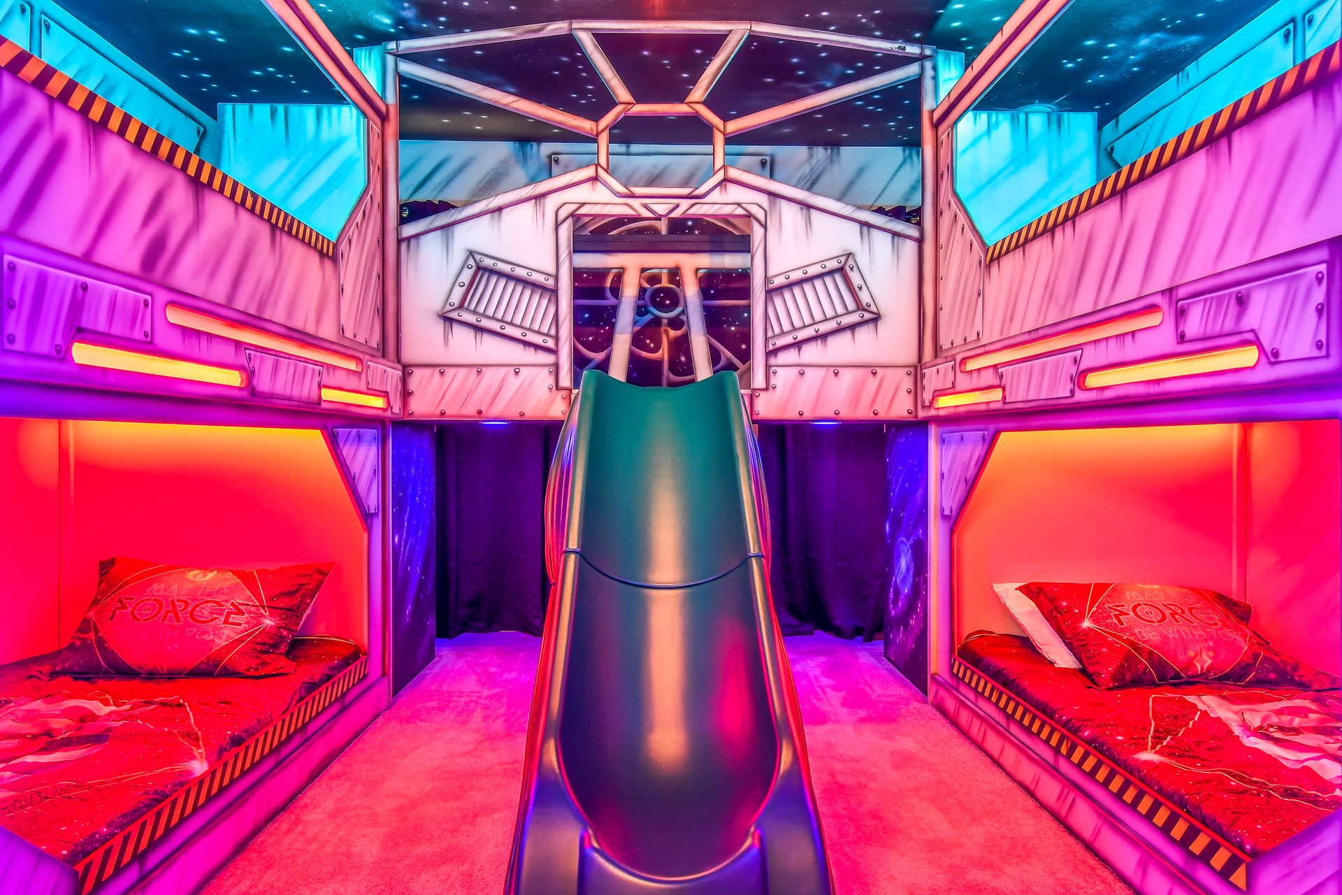 Futuristic space-themed bunk room with vibrant neon lighting, galactic decor, and a slide.