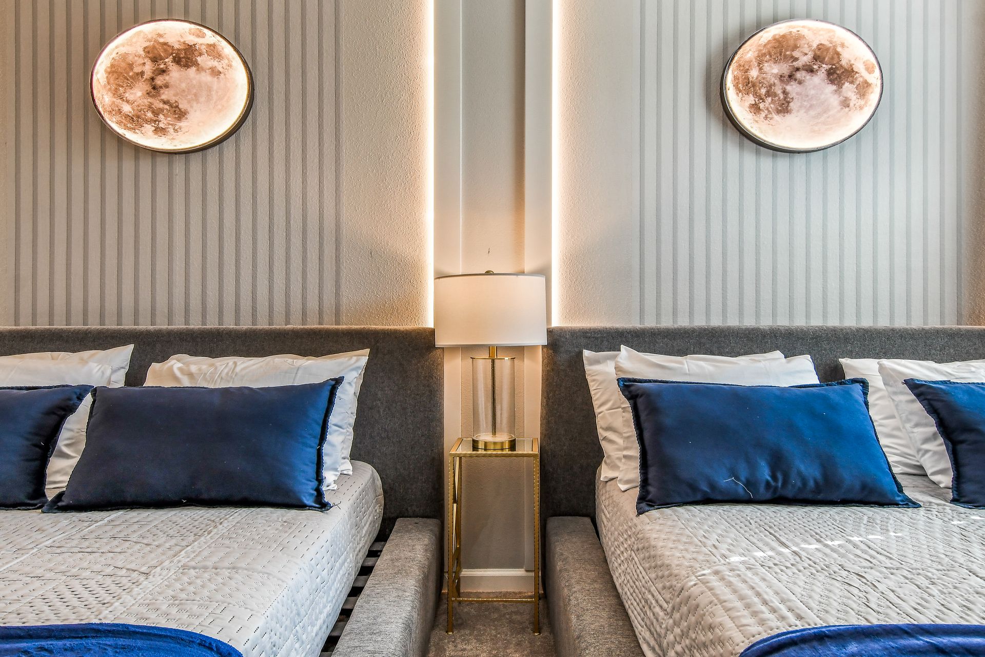 Chic bedroom with moonlit wall decor, plush blue pillows, and a sleek gold bedside lamp.