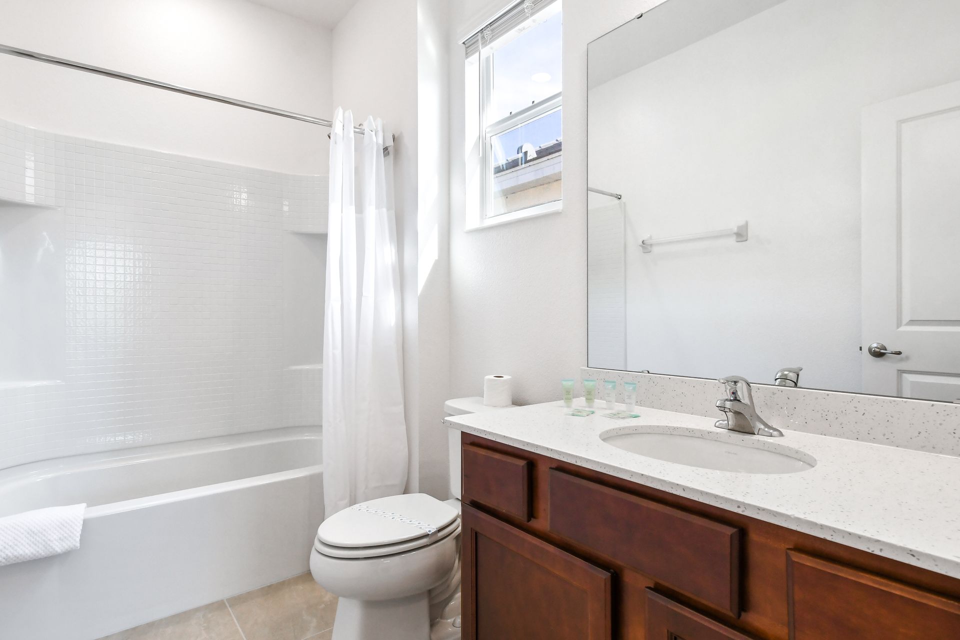 Bright and clean bathroom with a tiled shower-tub combo, modern vanity, and natural light.
