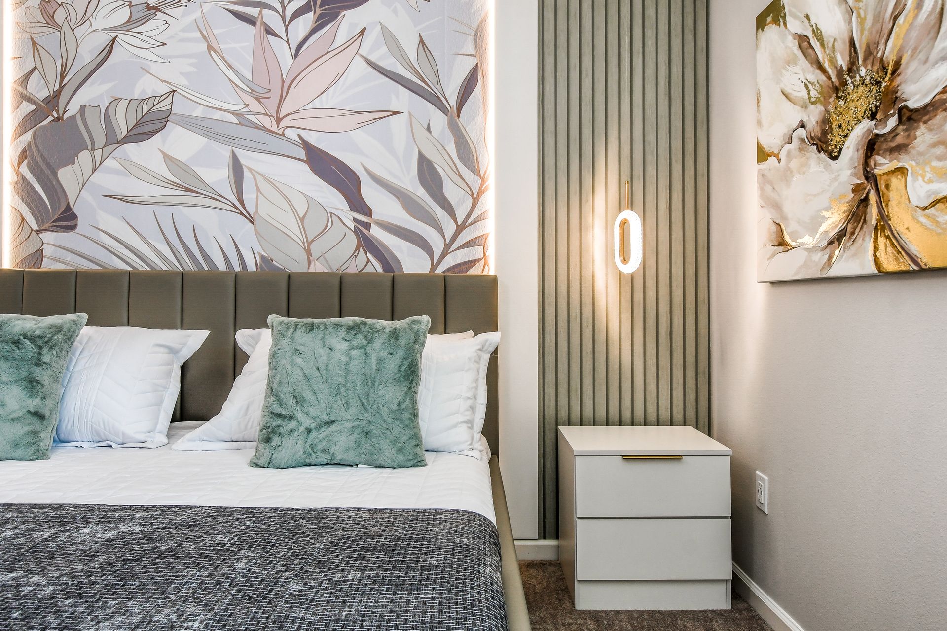 Stylish bedroom featuring botanical wallpaper, plush green pillows, and modern lighting accents.