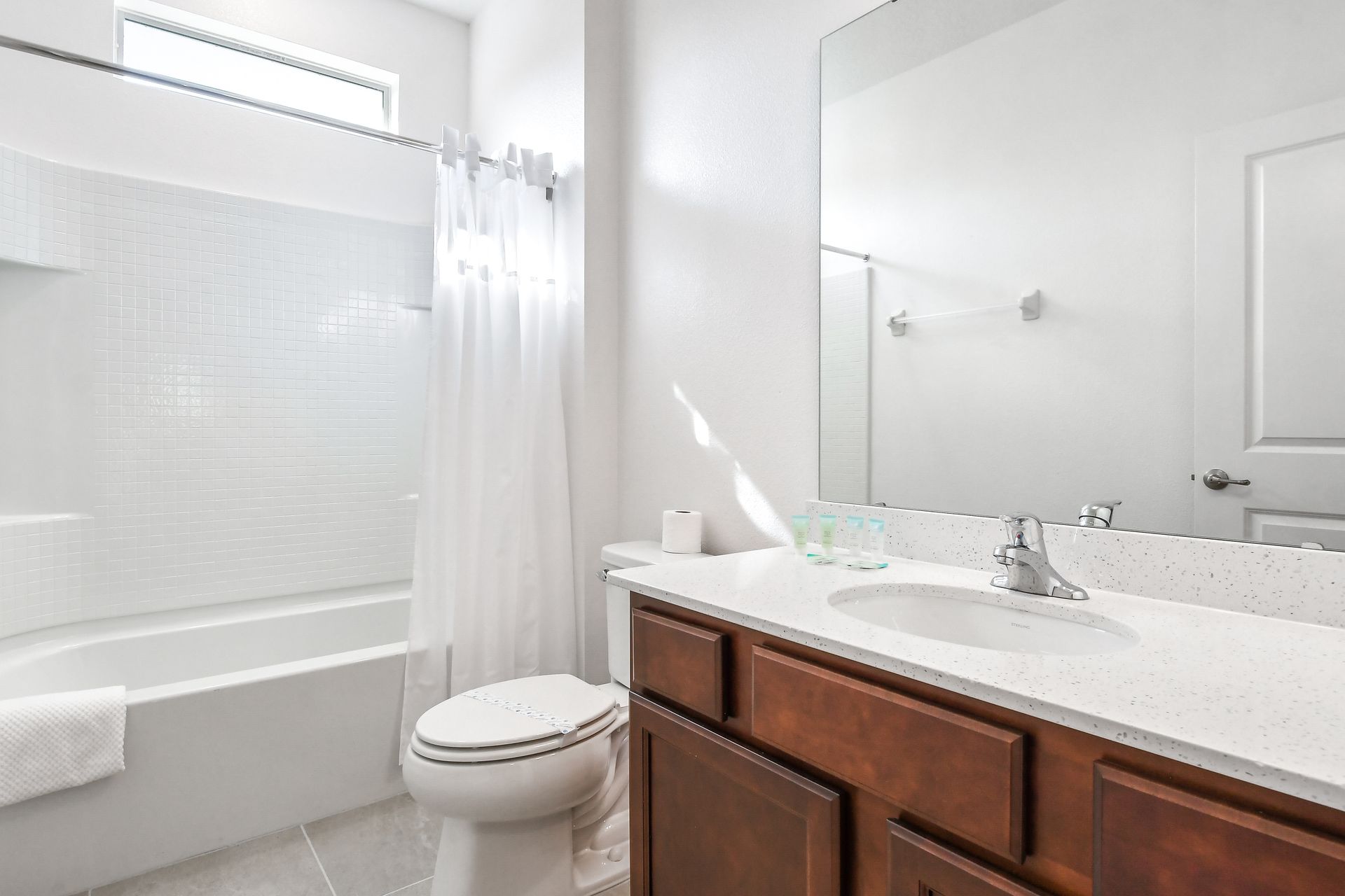 Bright bathroom with sleek quartz countertop, wooden cabinetry, and a tiled shower/tub.