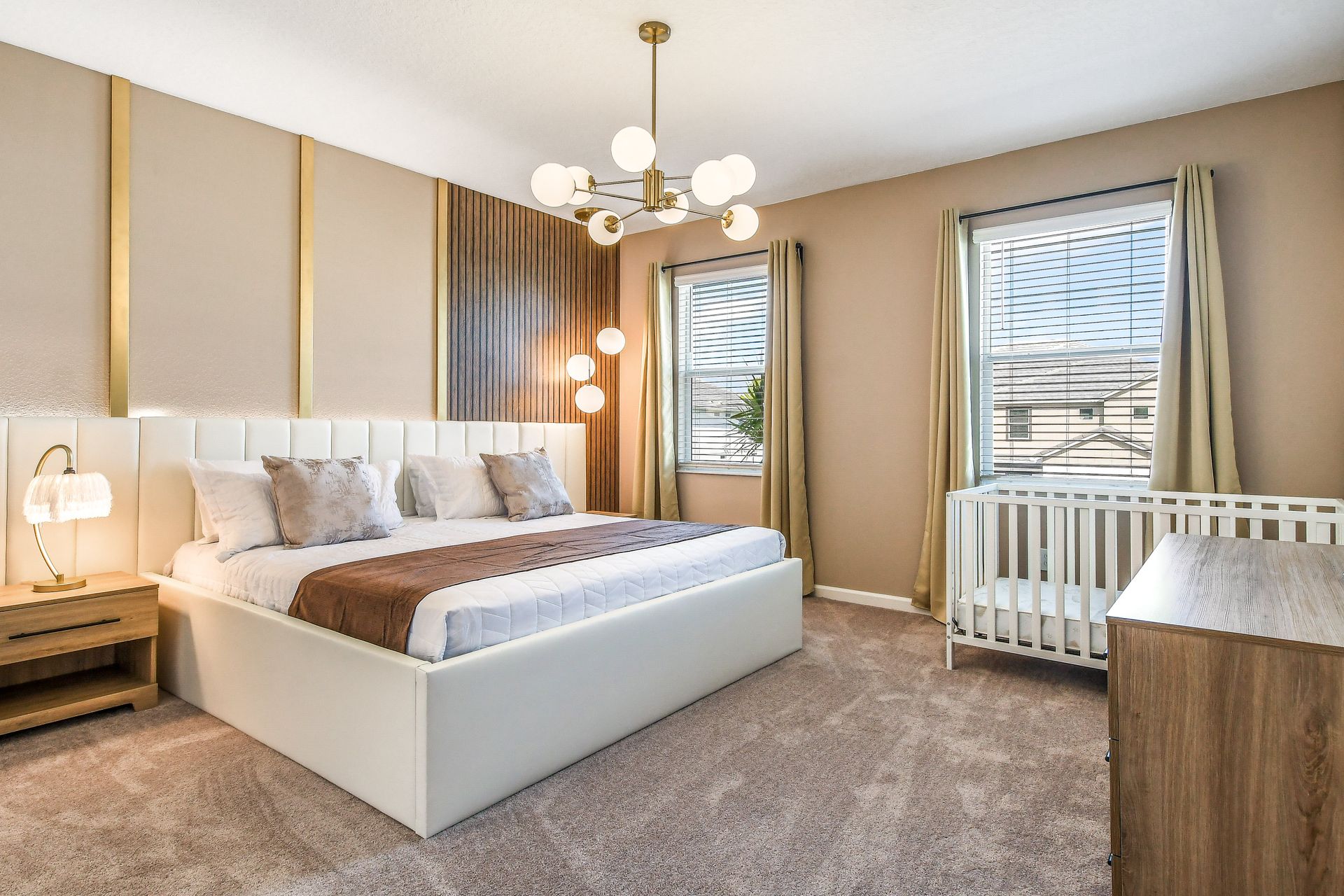 Luxurious bedroom with gold accents, tufted bed, chic chandelier, and cozy crib.