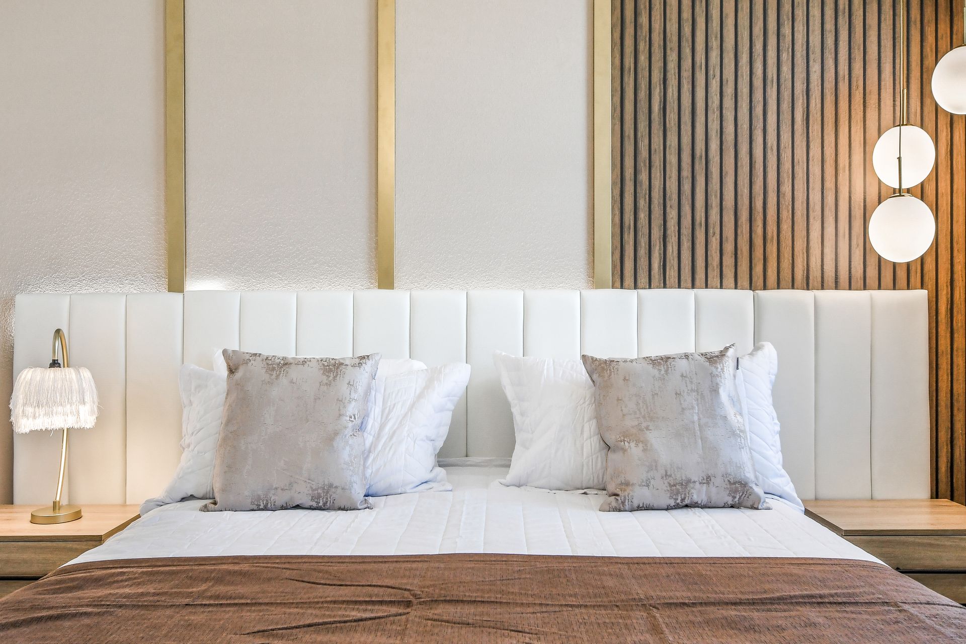 Elegant bed with a white tufted headboard, wood paneling, and modern lighting.