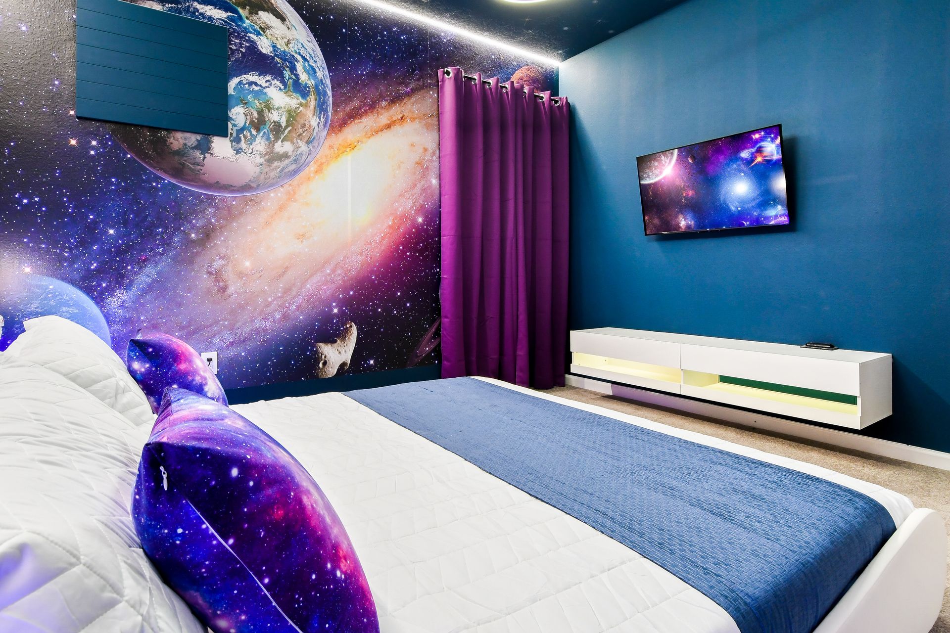 Sleek space-themed bedroom with galaxy pillows, cosmic murals, and a modern TV setup.