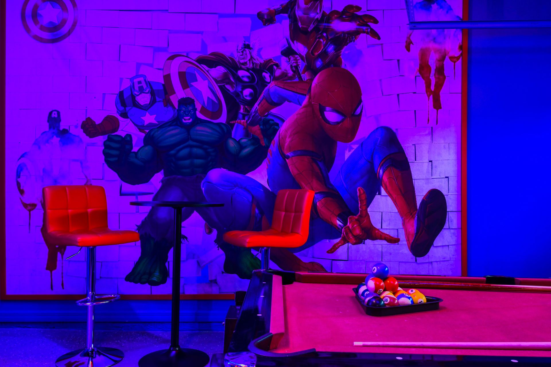 Superhero-themed game room with pool table, vibrant murals, and neon lighting!