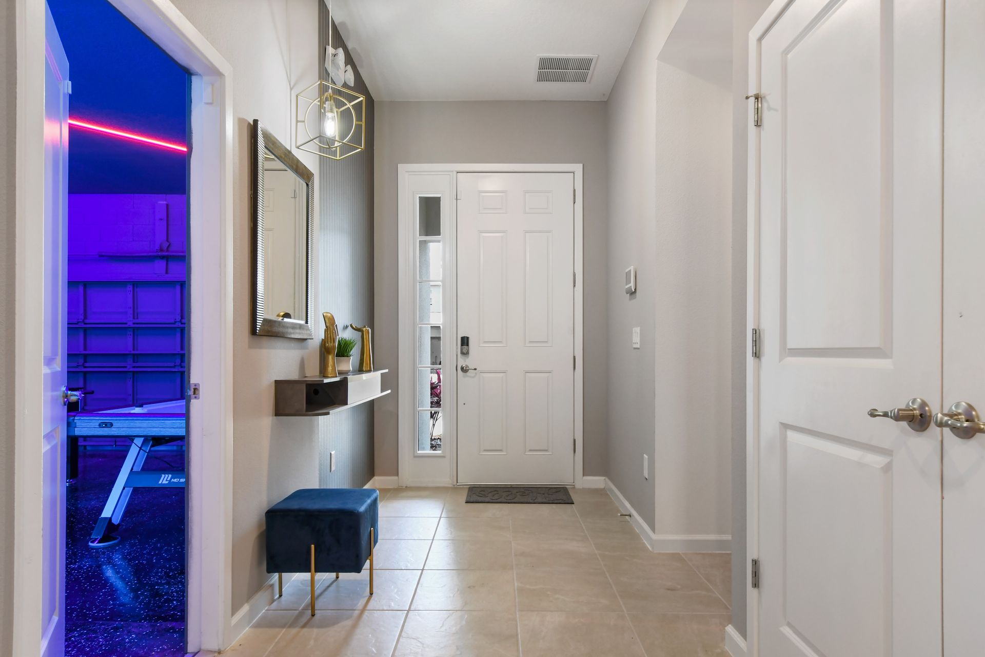 Stylish entryway with modern décor and a peek into the neon-lit game room.
