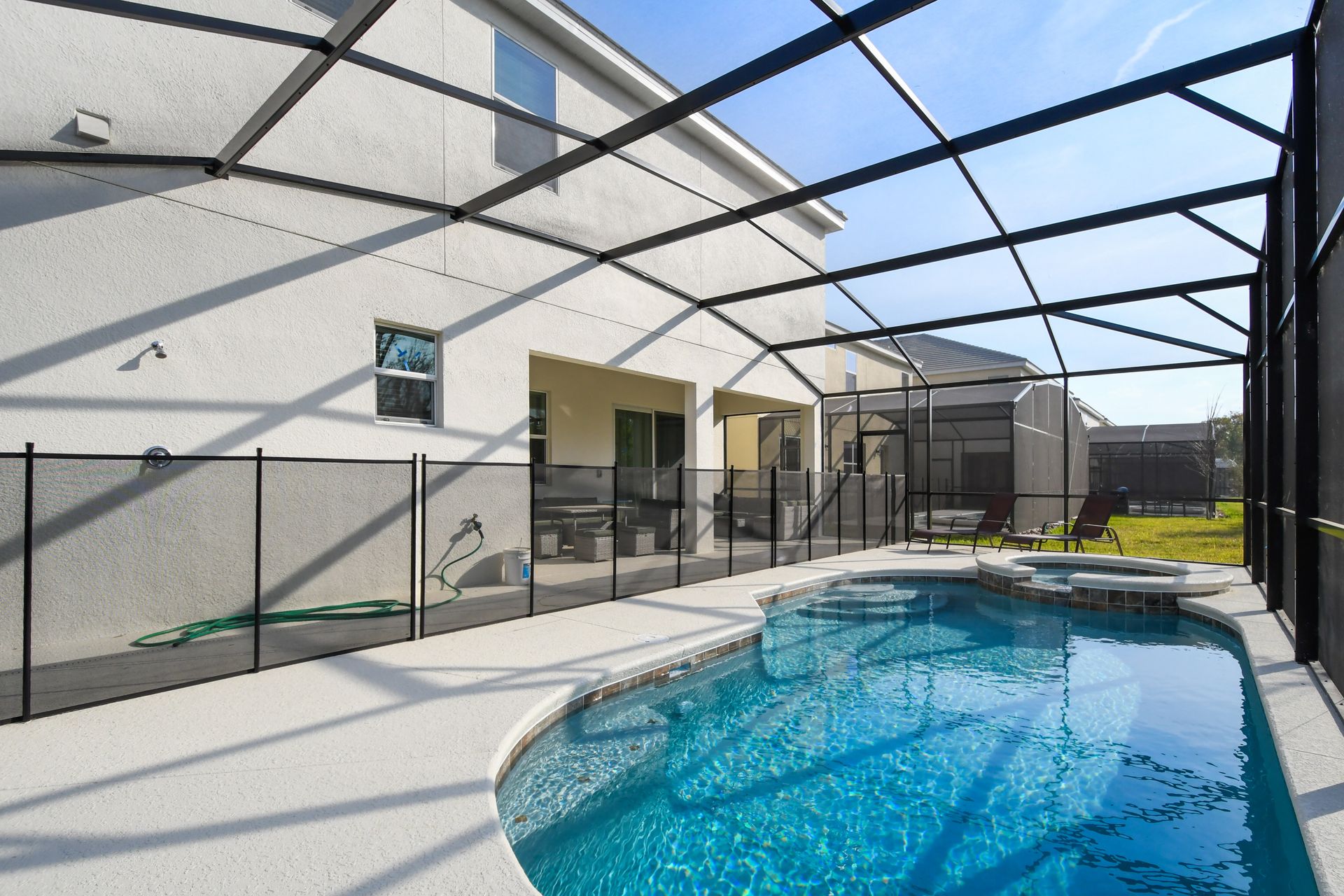 Private screened pool and spa with lounge chairs and shaded patio seating.
