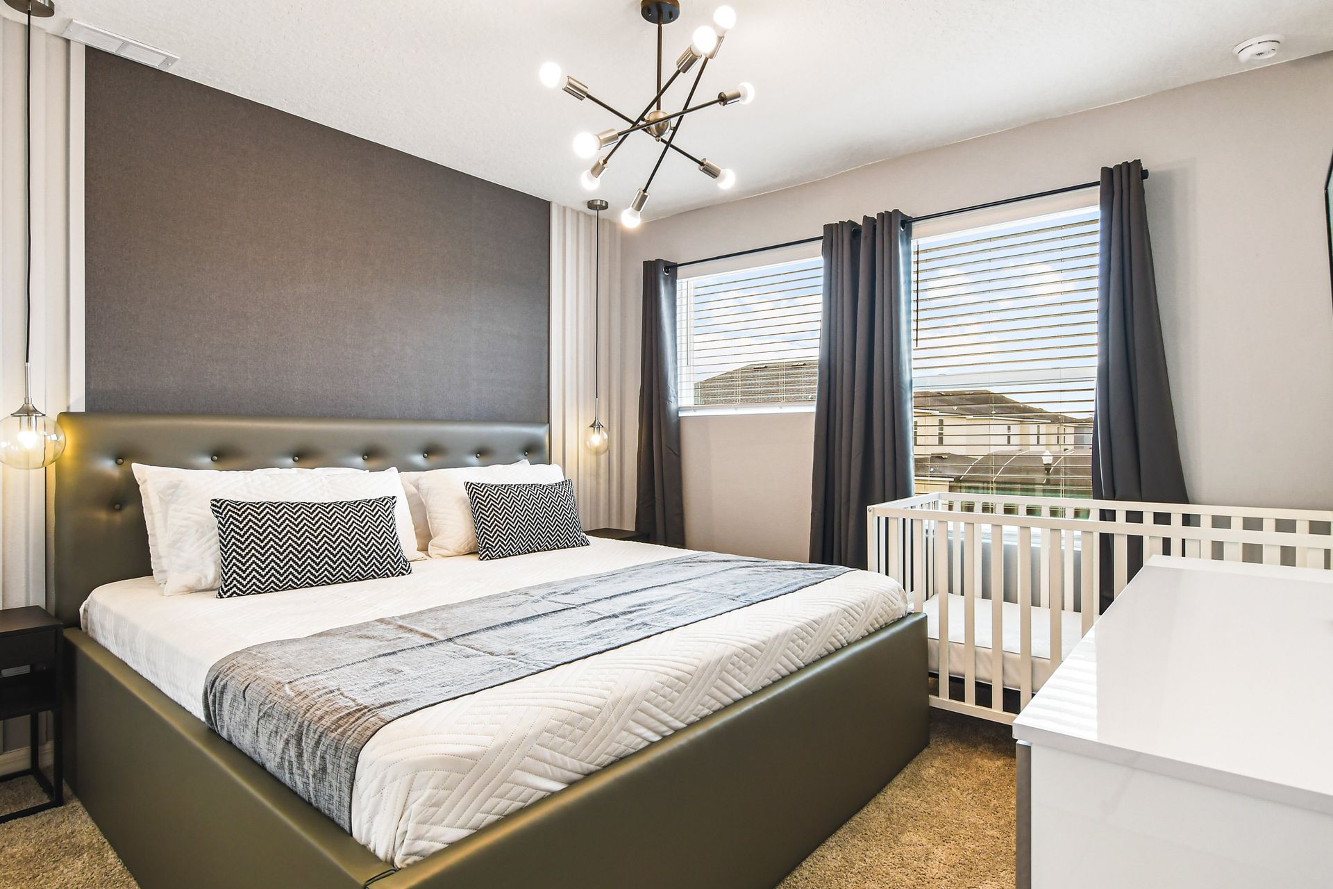 Relax in this modern king bedroom with a cozy crib and elegant lighting.