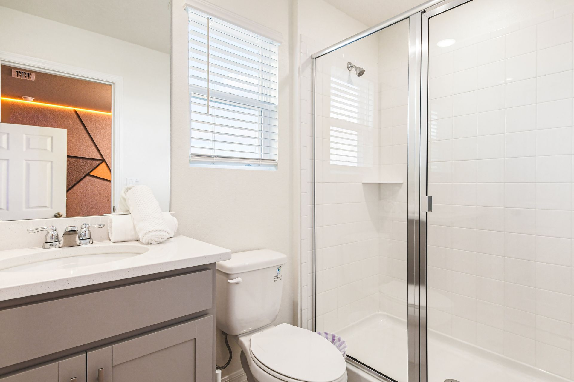 Bright bathroom with glass shower, sleek vanity, and modern fixtures.