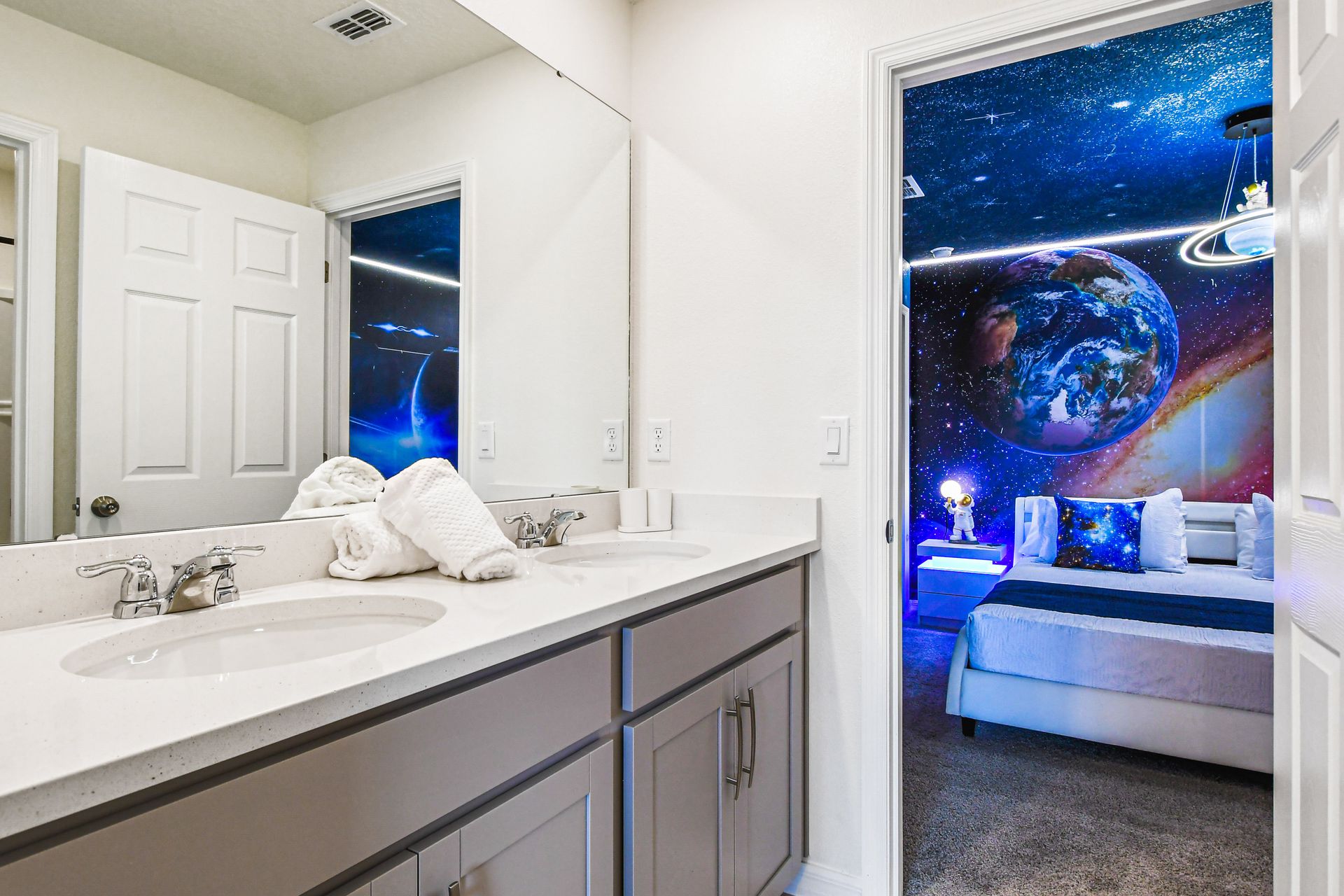 Modern bathroom with double vanity, sleek design, and a view into a space-themed room.