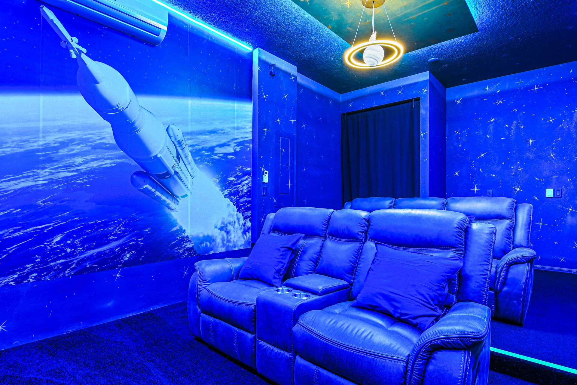 Space-themed theater room with reclining seats, starry walls, and ambient lighting.