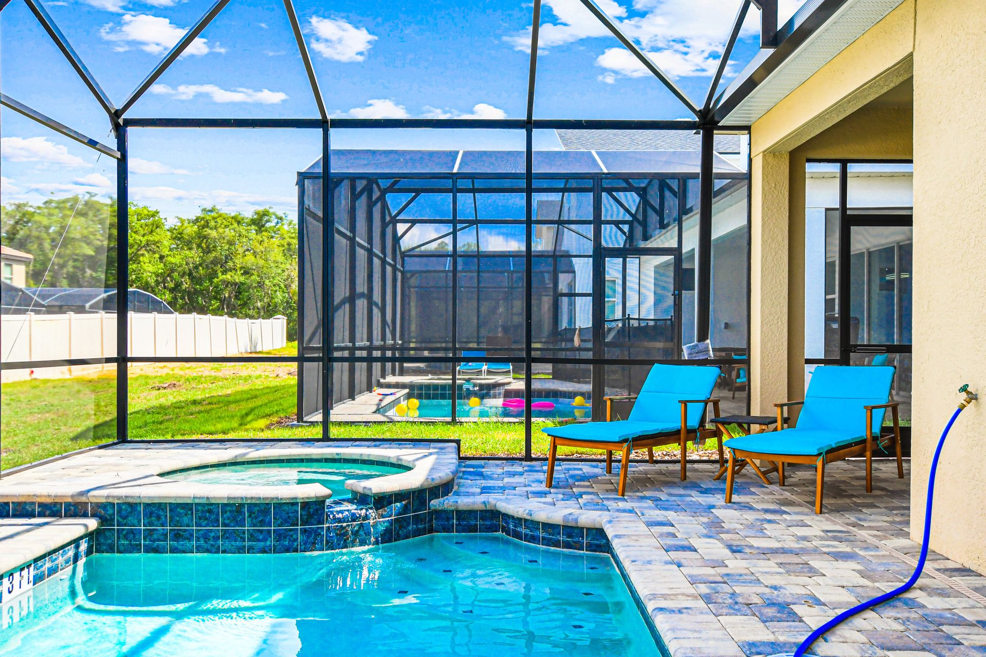 Screened pool and spa with lounge chairs, sunny views, and paved patio.