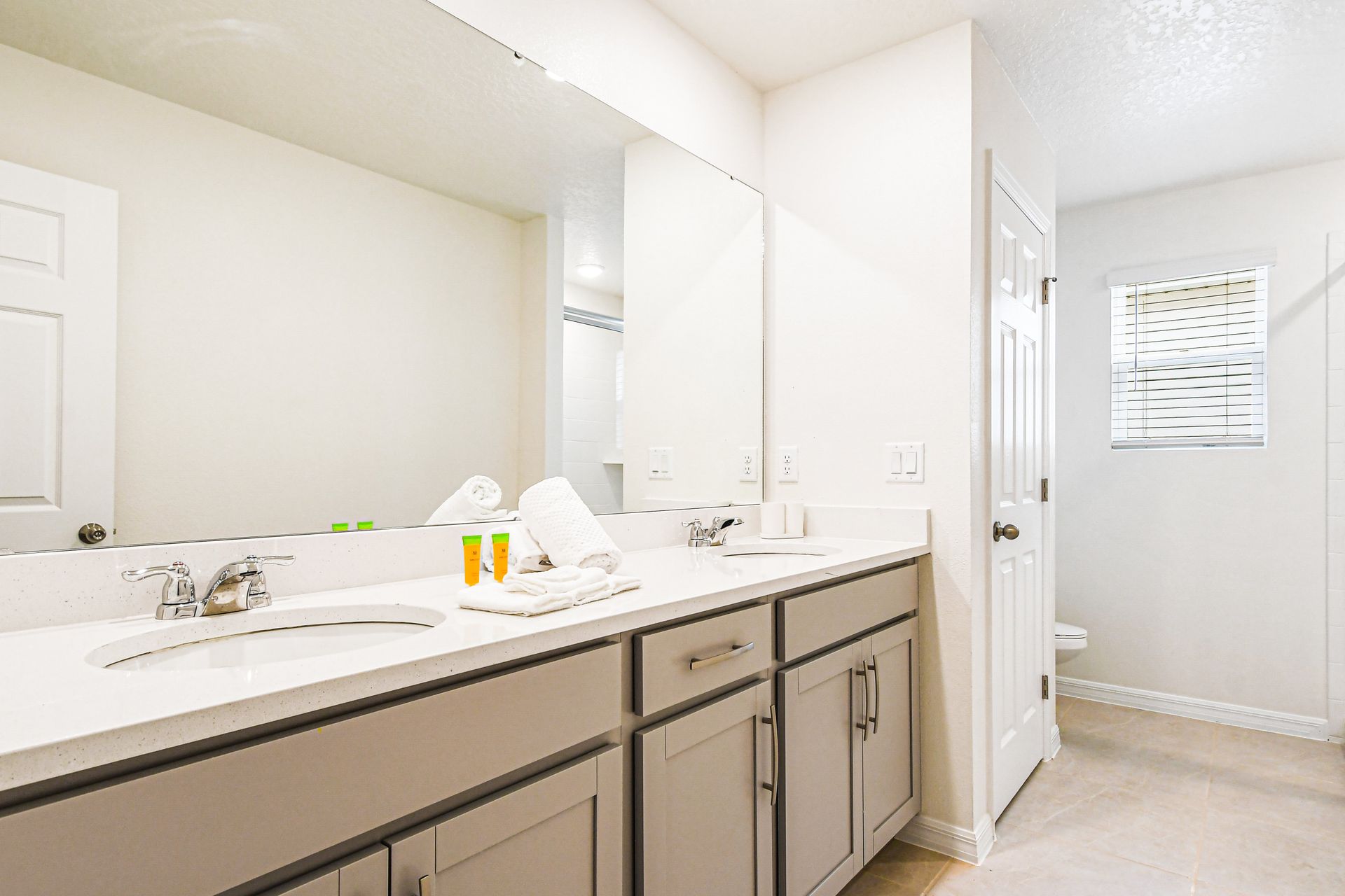Spacious bathroom with dual sinks, large mirror, and bright natural lighting.