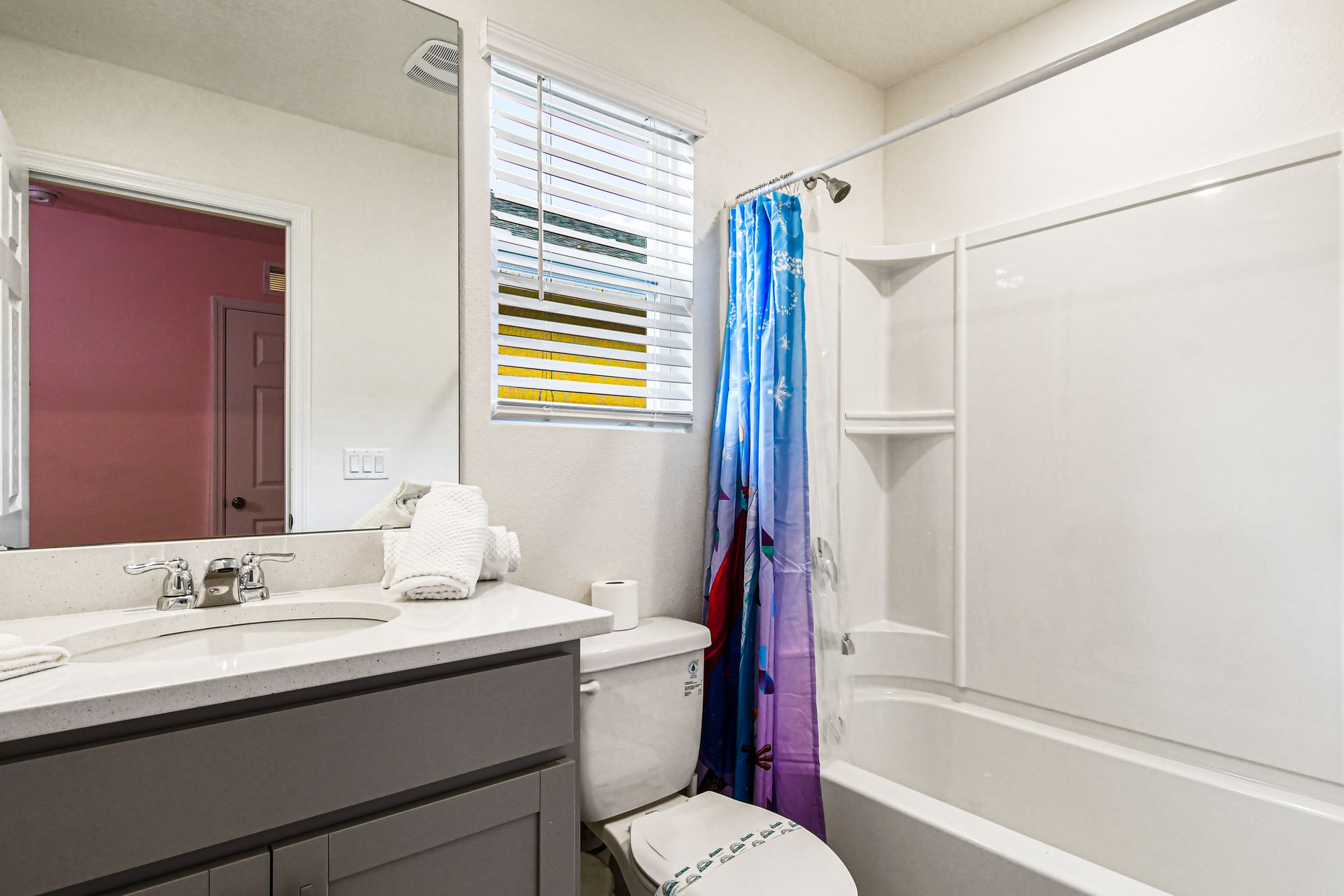 Bright bathroom with themed shower curtain, modern vanity, and natural light.
