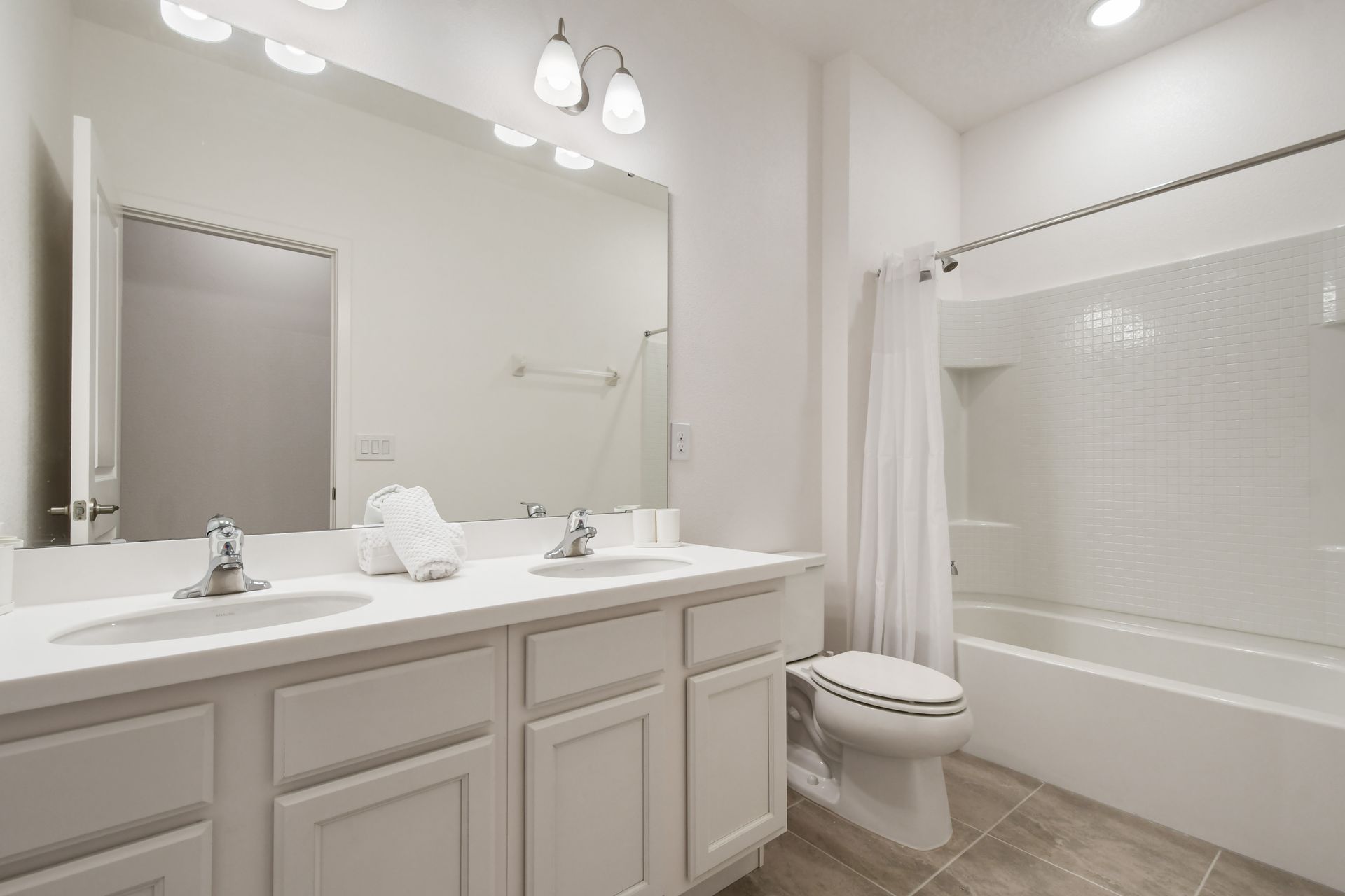Bright and clean bathroom with a large mirror and a full shower-tub combo.