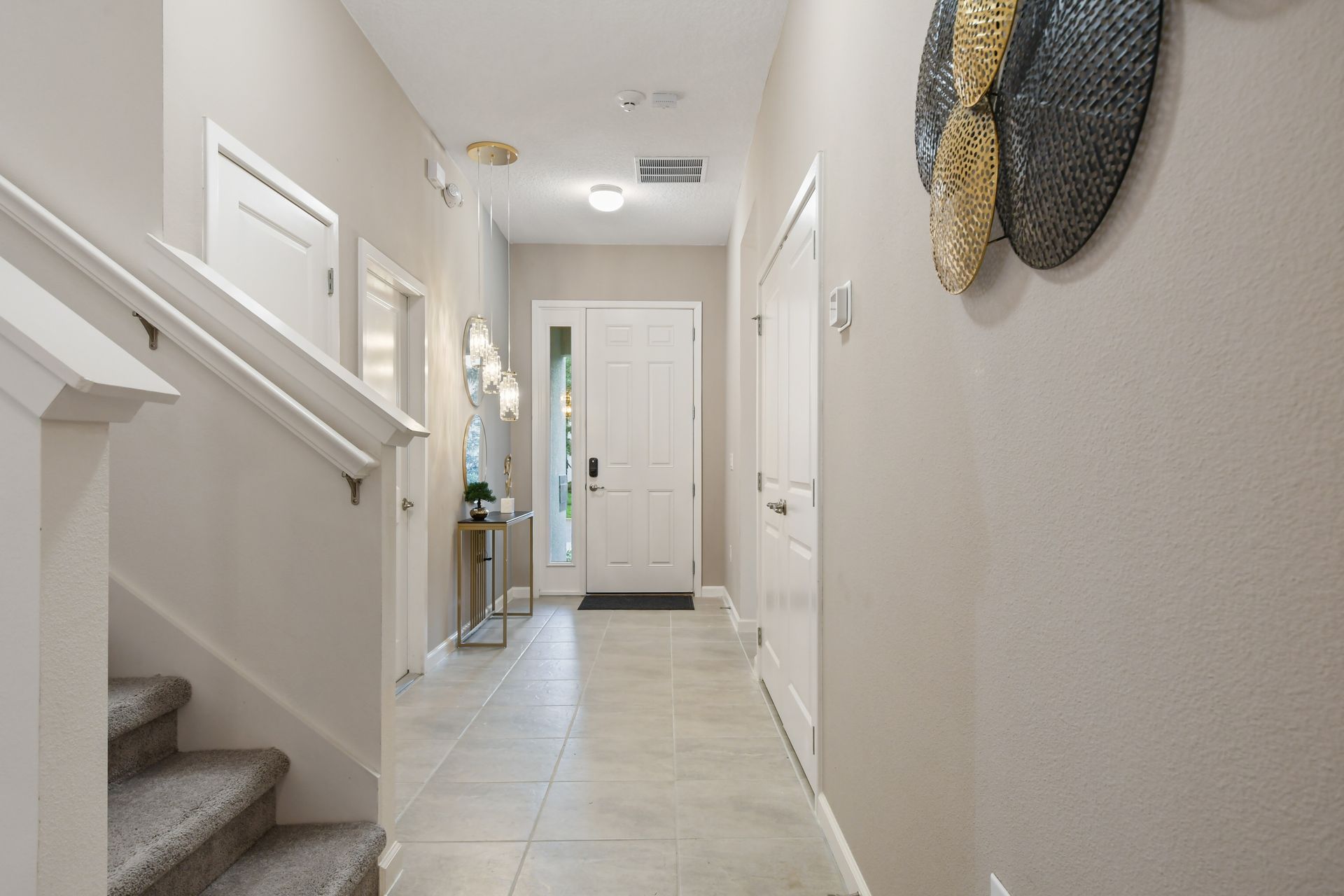 Welcoming foyer with modern pendant lights, elegant décor, and neutral tile floors
