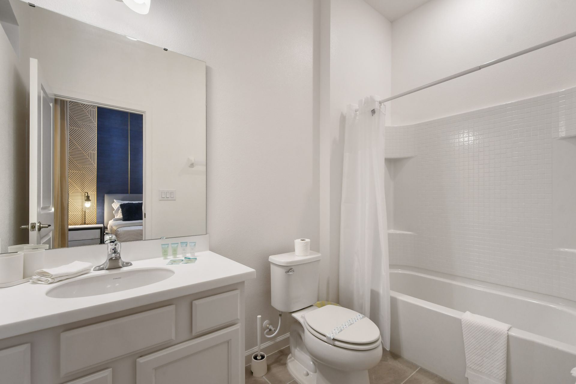 Ensuite bathroom with sleek white finishes, large mirror, and full tub-shower combo
