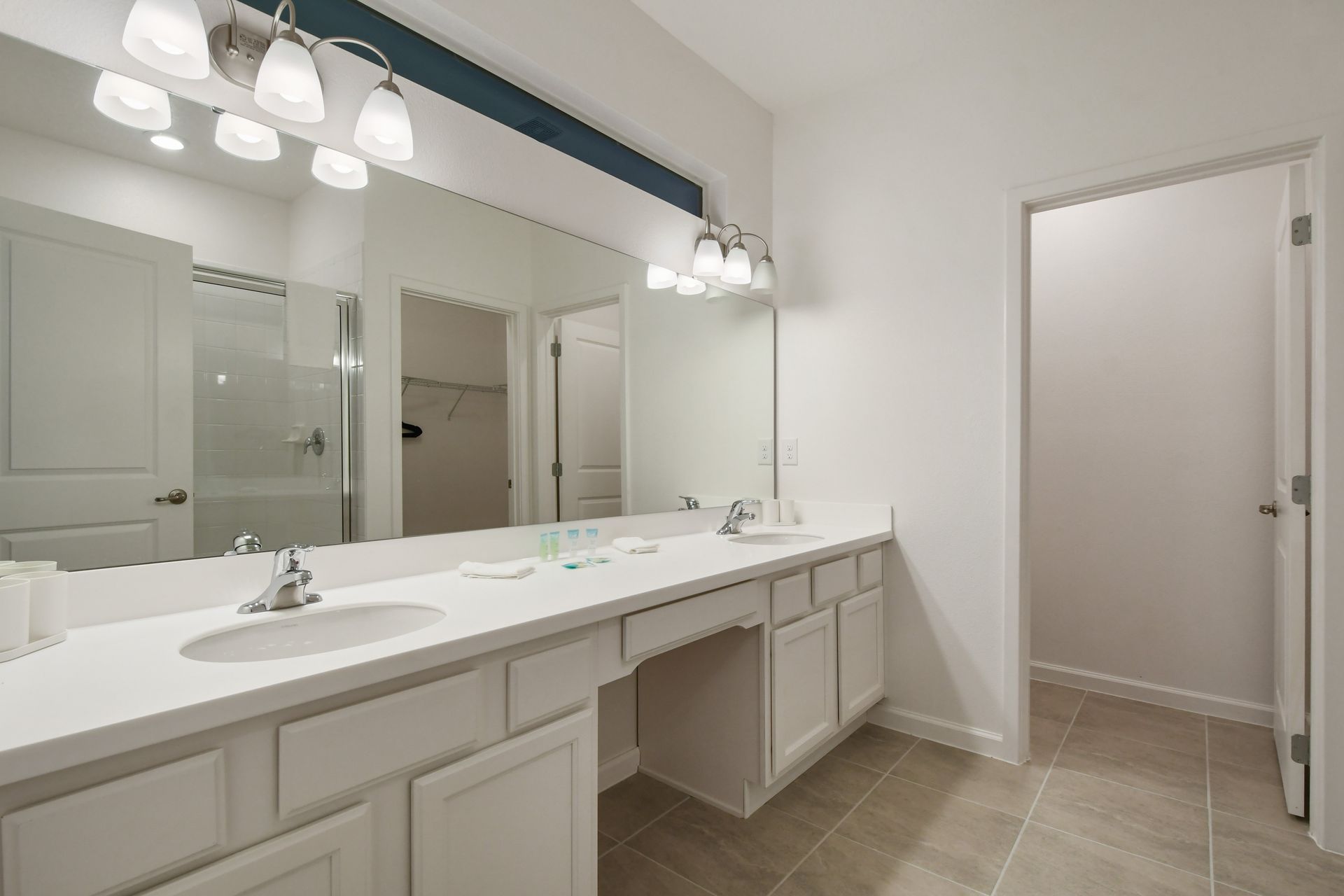 Elegant master bathroom with dual sinks, vanity seating, and walk-in closet access
