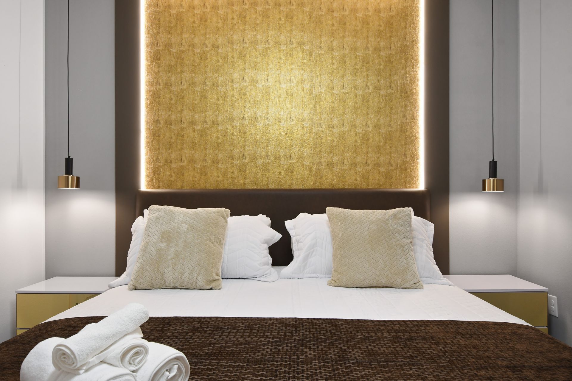 Modern bedroom with gold accents, plush king bed, and striking statement lighting
