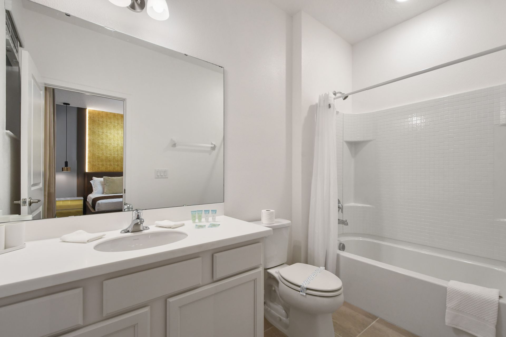 Bright and modern bathroom featuring a sleek vanity, full mirror, and combination bathtub with white tile surround