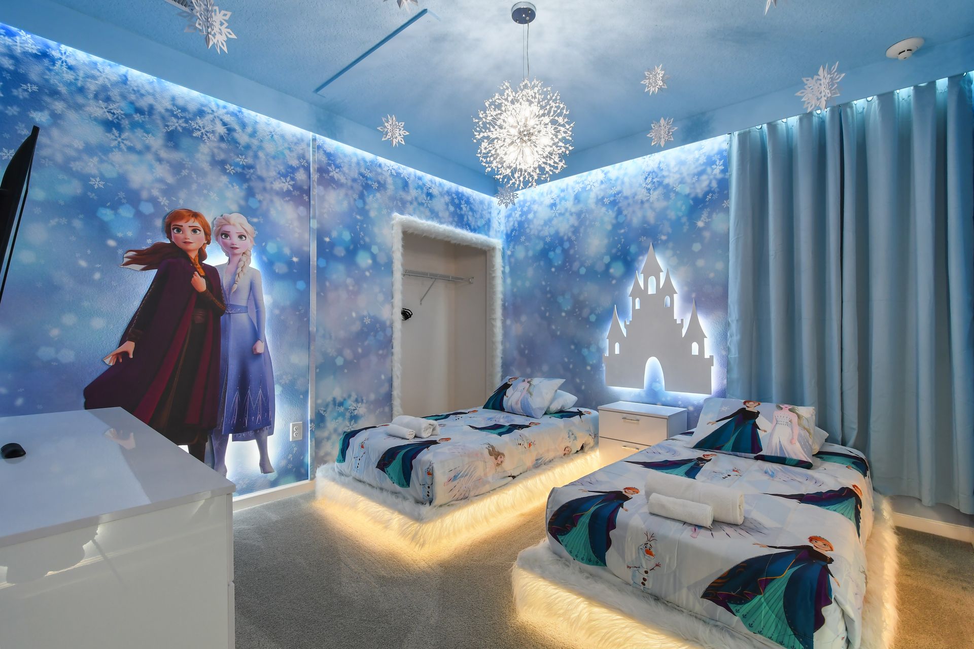 Frozen-themed bedroom with glowing beds, snowflake lights, and magical castle mural
