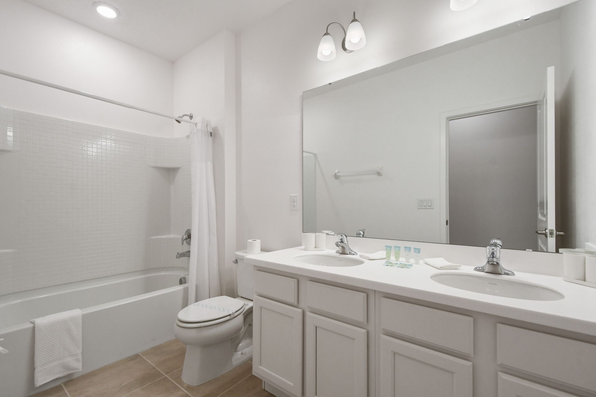Bright and clean full bathroom with double vanity, large mirror, and tub-shower combo
