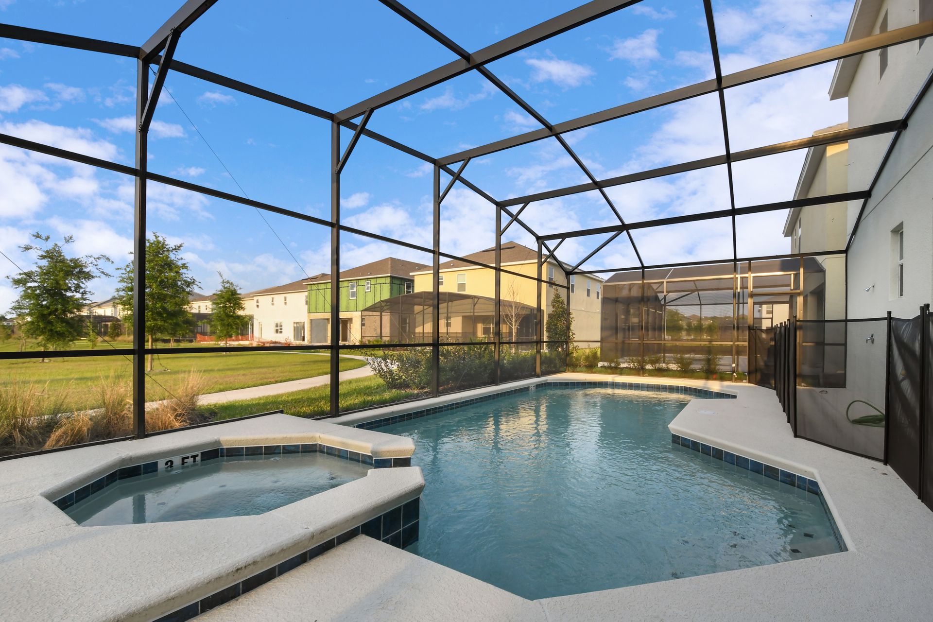 Screened-in pool with spa overlooking a serene lake and lush greenery.